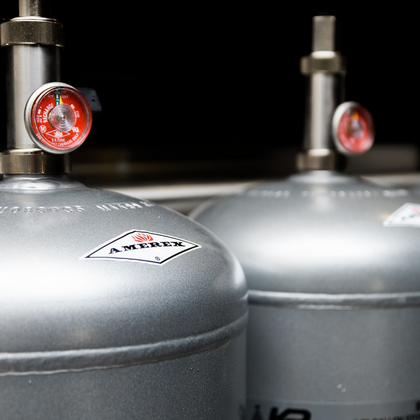 Close-up of two silver Amerex fire extinguisher tanks with pressure gauges, positioned side by side in an indoor setting.