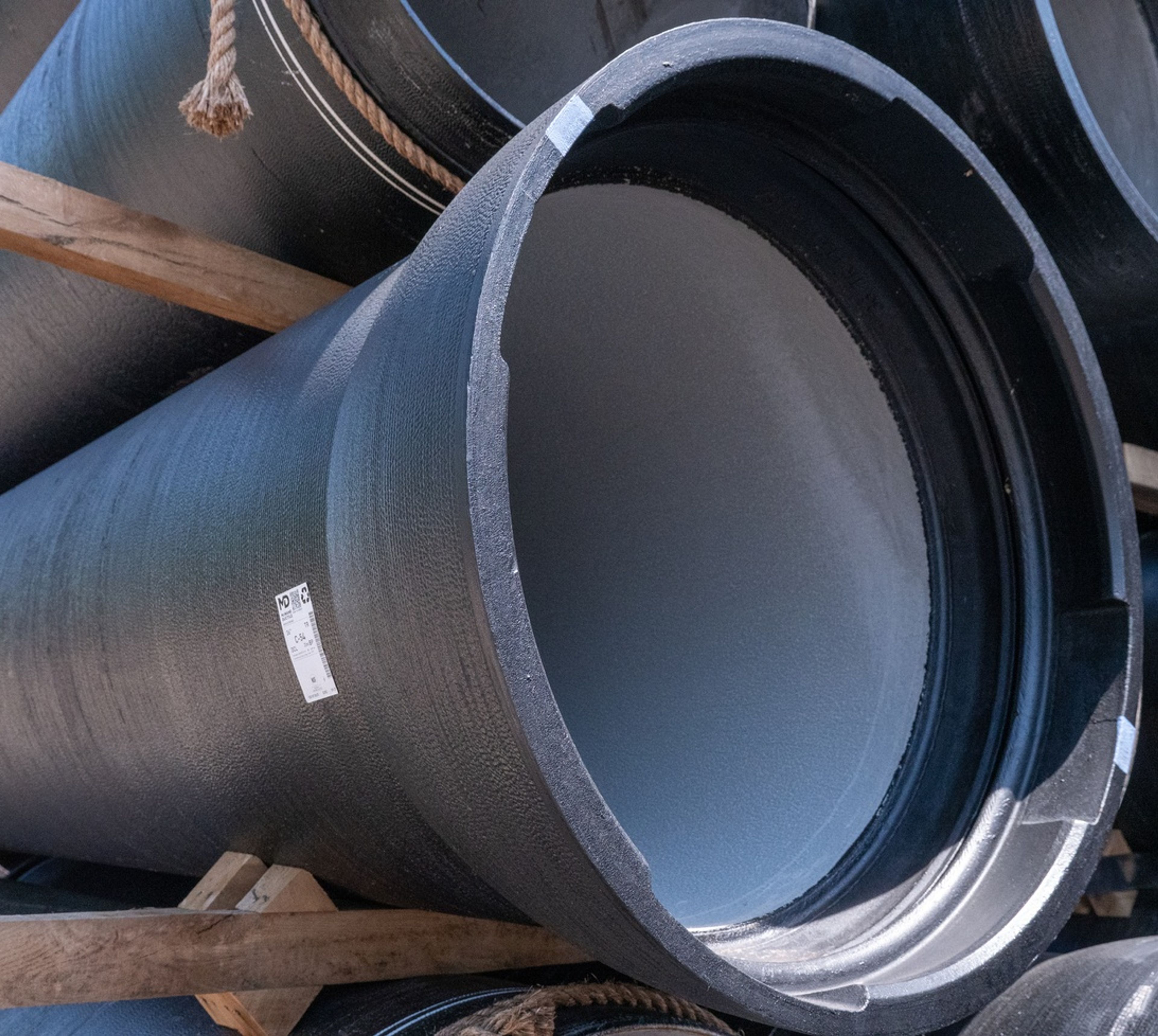 A close-up view of large black industrial pipes stacked on wooden supports, with a white label visible on one pipe.