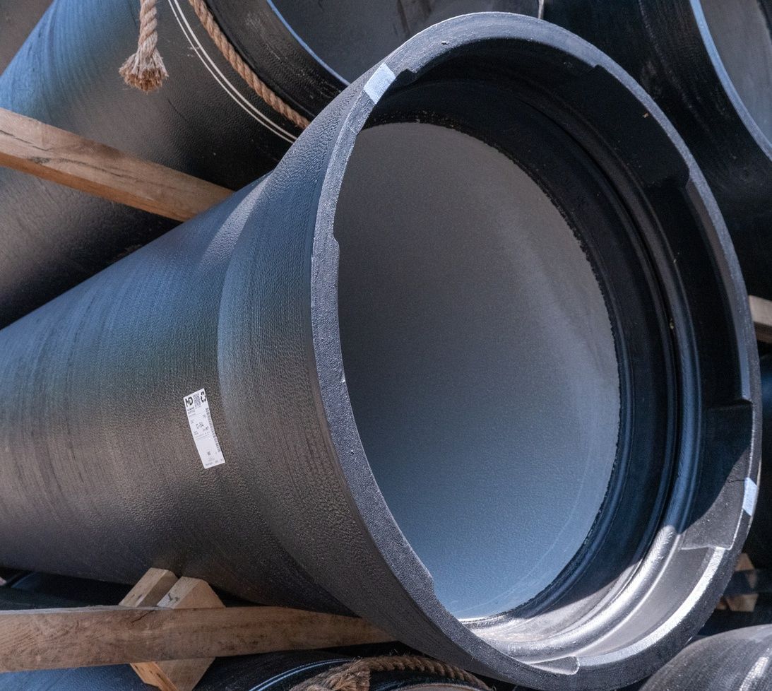 A close-up view of large black industrial pipes stacked on wooden supports, with a white label visible on one pipe.