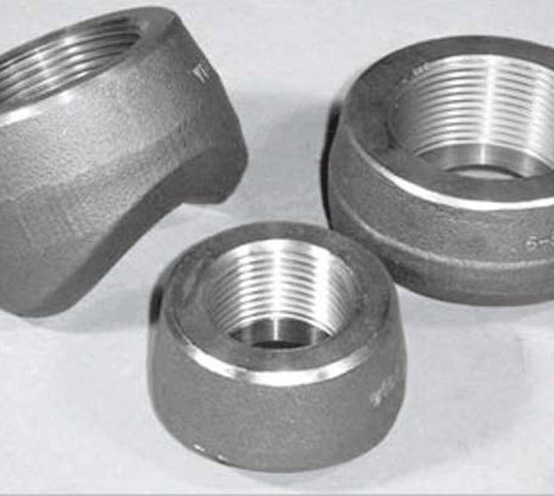 Three metallic pipe fittings with threaded interiors, placed on a light surface. Two are upright, showing the threading inside, while one fitting is tilted, revealing its shape and partial threads.