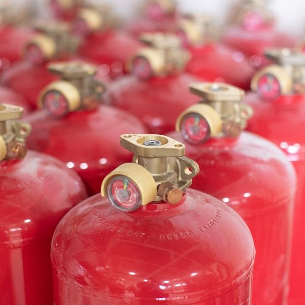 Close-up of several red fire extinguishers with brass-colored valves and pressure gauges, arranged closely together in rows.