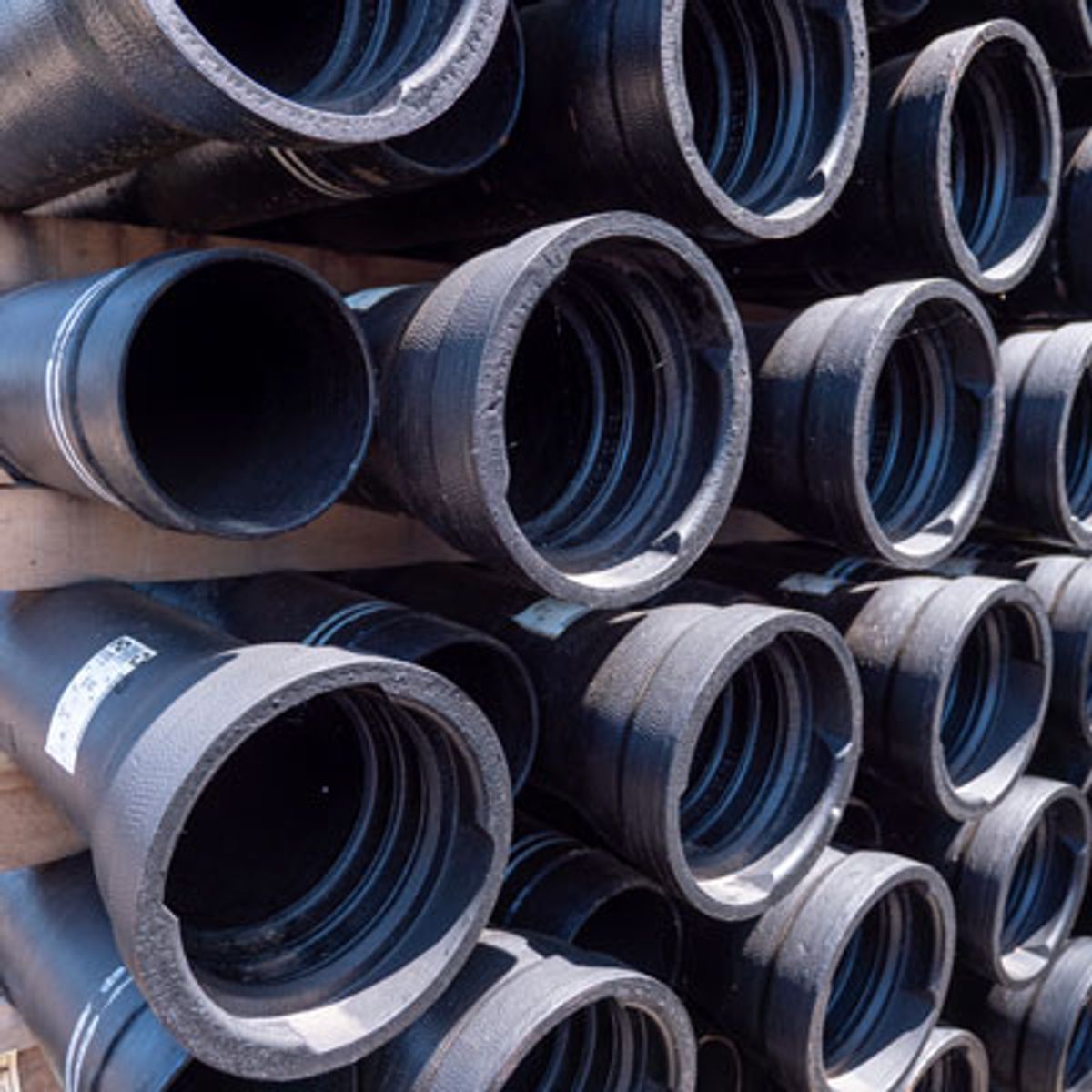 A close-up of stacked black metal pipes arranged in rows, showing the open ends facing outward, with visible threading inside the pipes.