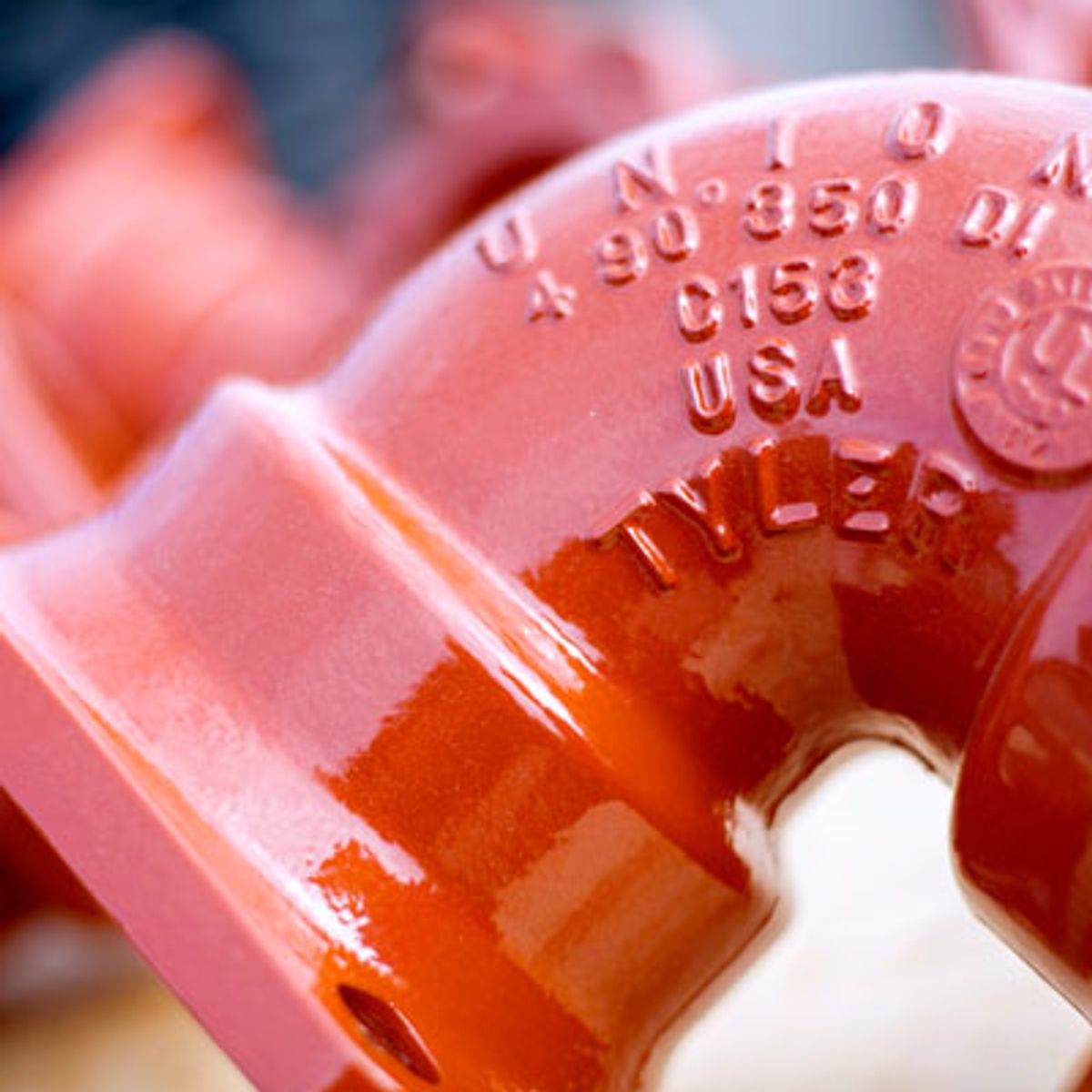 Close-up of a red metal pipe fitting with embossed text including “UNION,” “C153,” “USA,” and “TYLER.” The text and smooth, glossy surface are in focus, highlighting details of the pipe piece.
