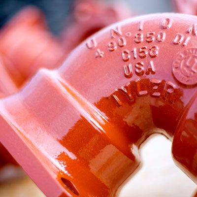 Close-up of a red metal pipe fitting with embossed text including “UNION,” “C153,” “USA,” and “TYLER.” The text and smooth, glossy surface are in focus, highlighting details of the pipe piece.