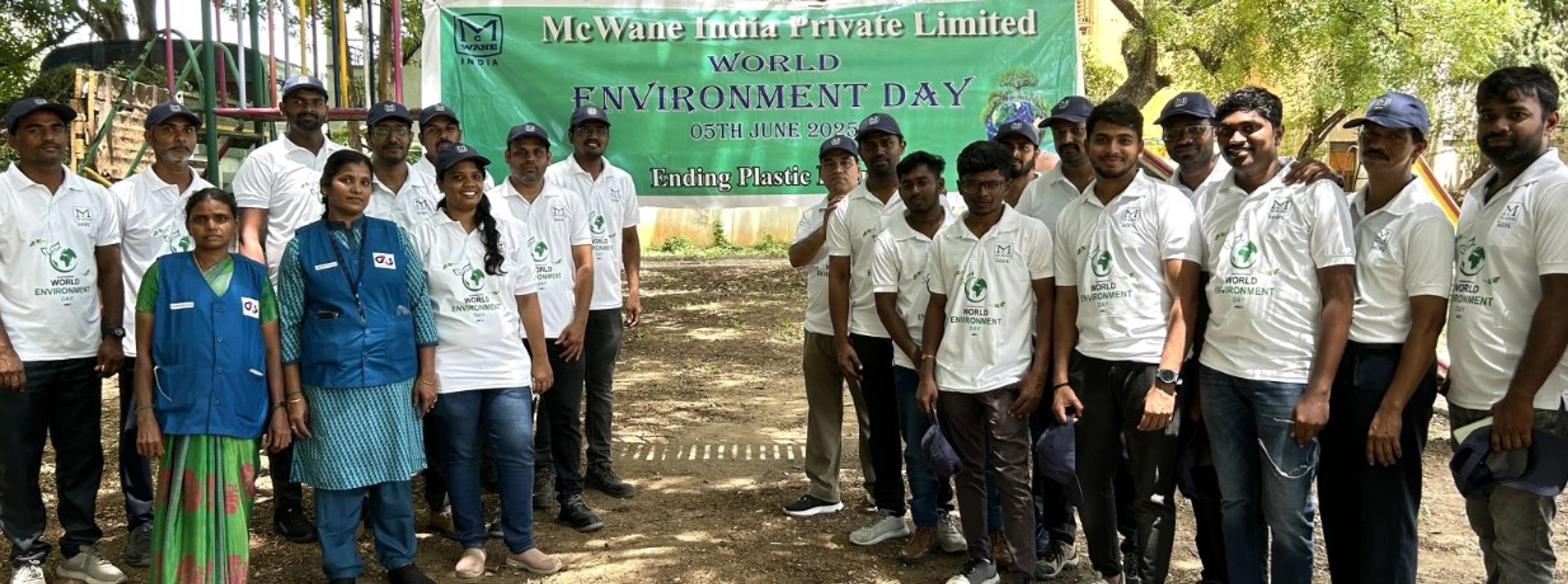 A group of people pose outdoors in front of a green World Environment Day banner that reads “Ending Plastic,” wearing uniforms and caps, during a company-sponsored event.
