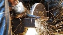 A close-up of a person using an angle grinder on metal, with bright sparks flying in various directions.