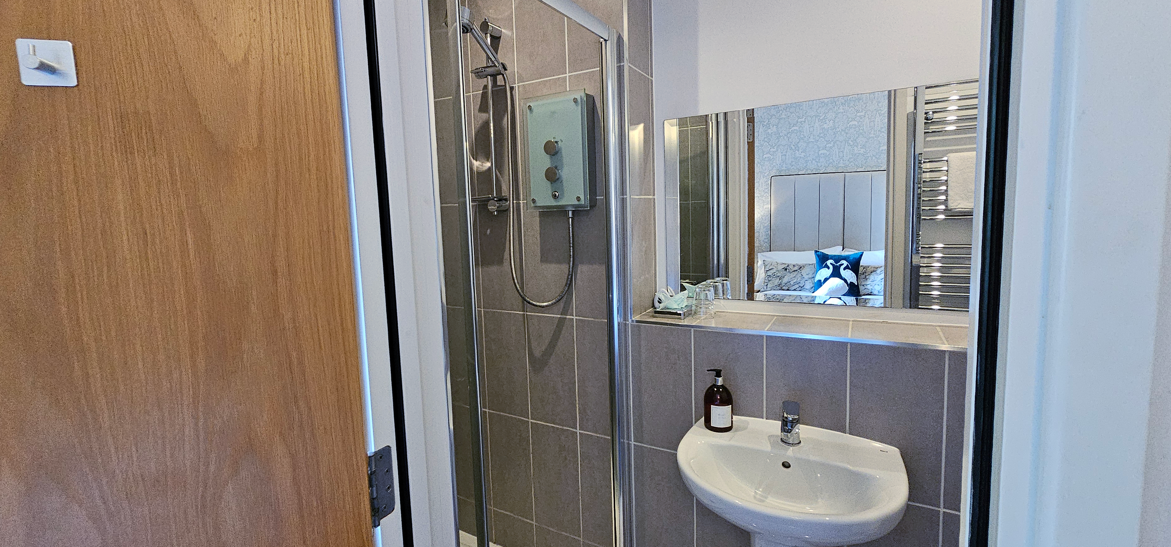 Double bed with panelled headboard shown in mirror of the ensuite bathroom with shower