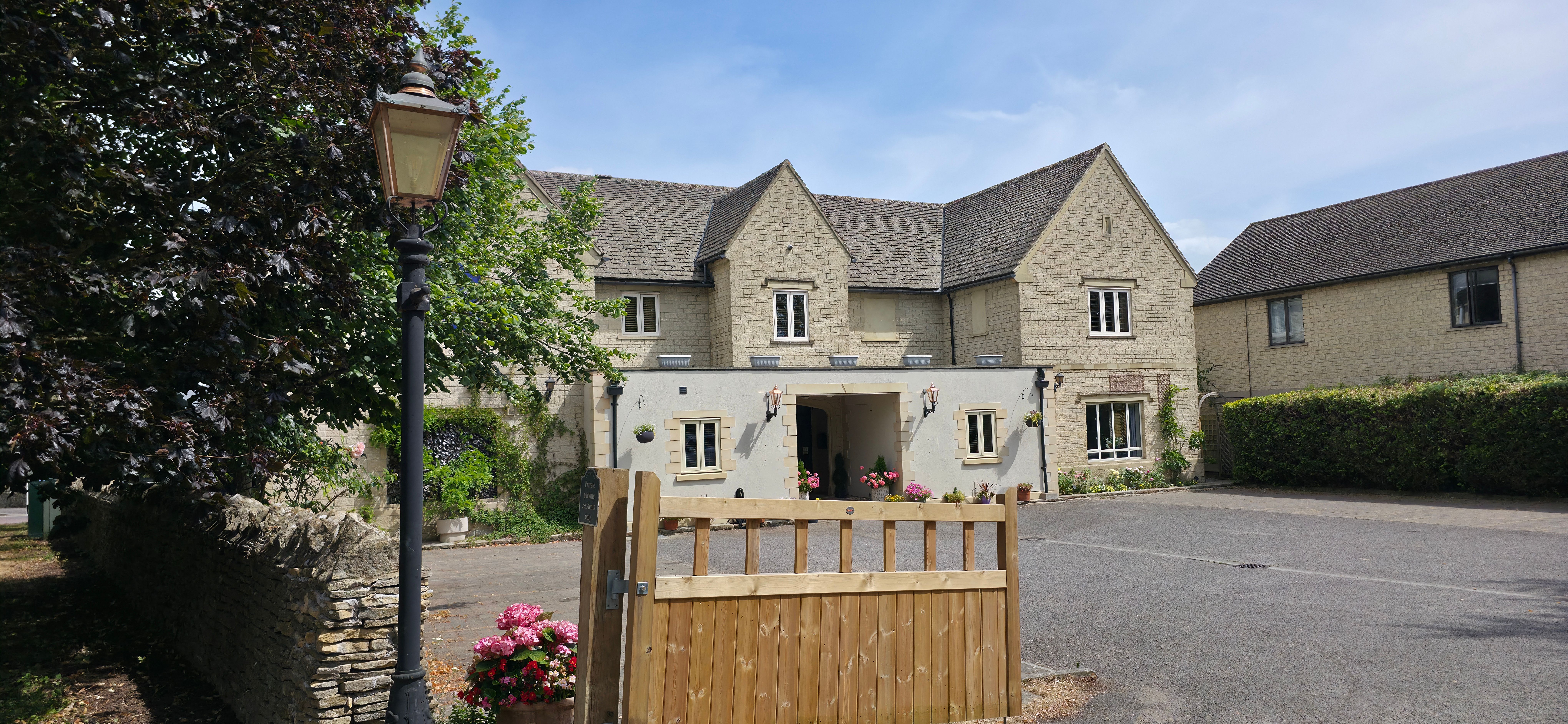 Timber gate and lamp post in front of a stone building with porch entrance