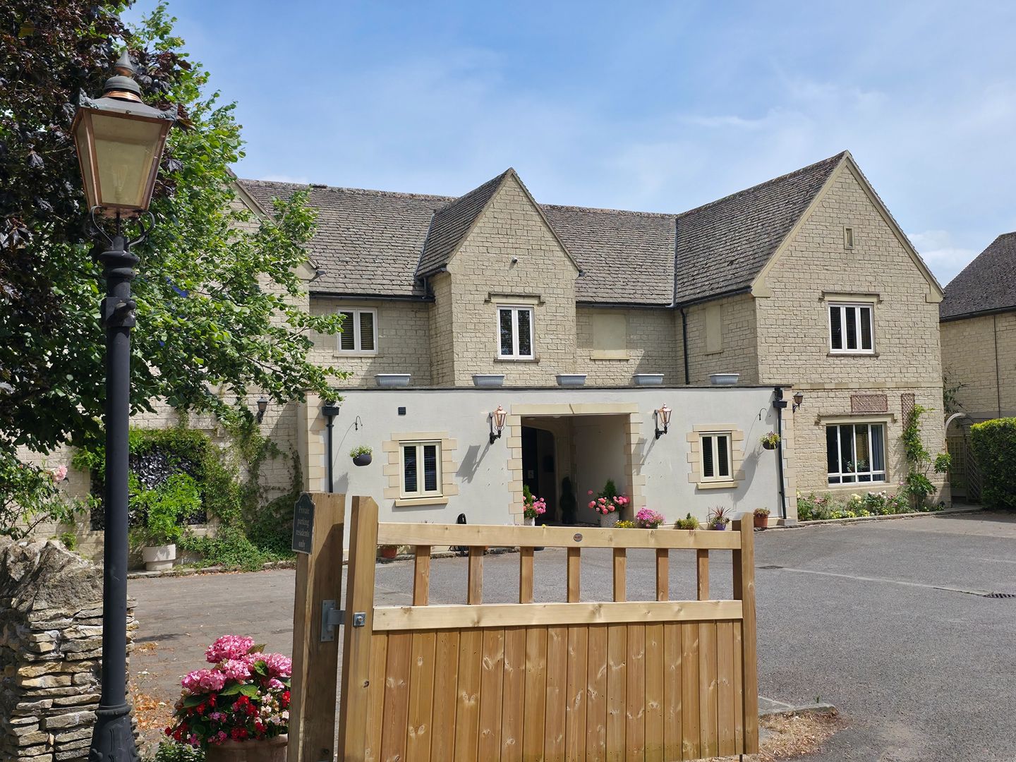 Timber gate and lamp post in front of a stone building with porch entrance