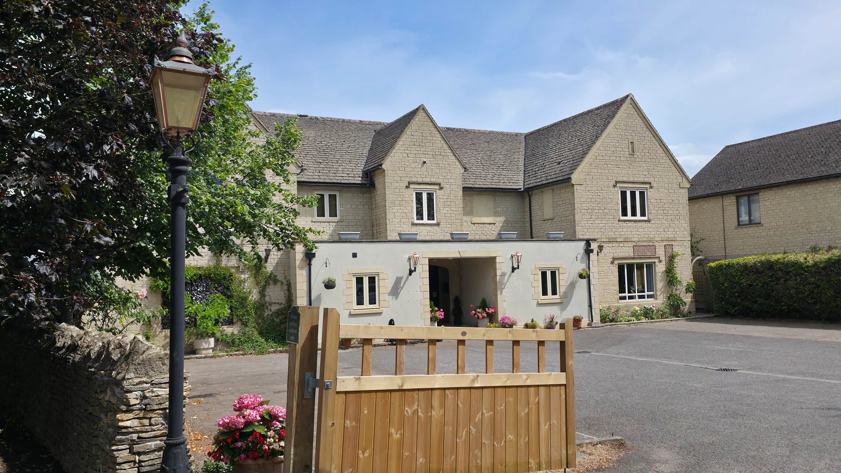 Timber gate and lamp post in front of a stone building with porch entrance