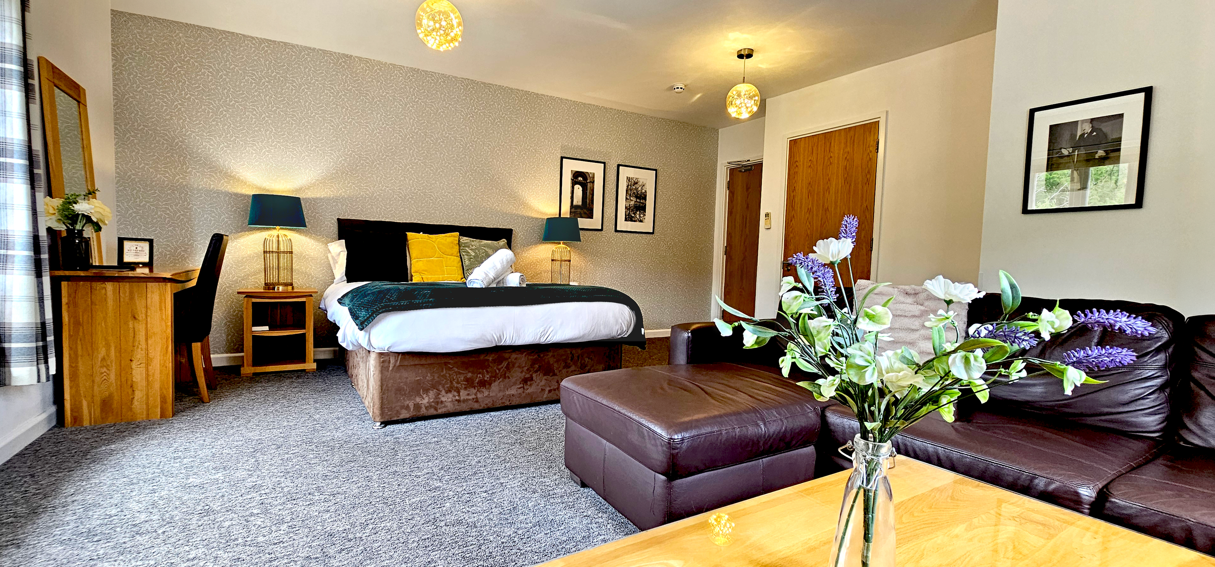 Deluxe king size bed with green throw, rolled towels & matching teal lamps on oak bedside tables