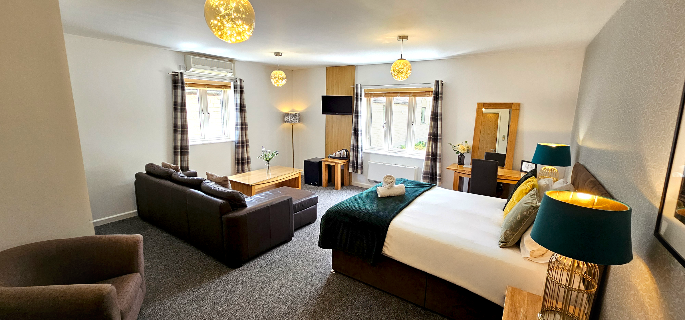 Large deluxe room with king size bed, green throw, leather sofa, armchair and checked curtains