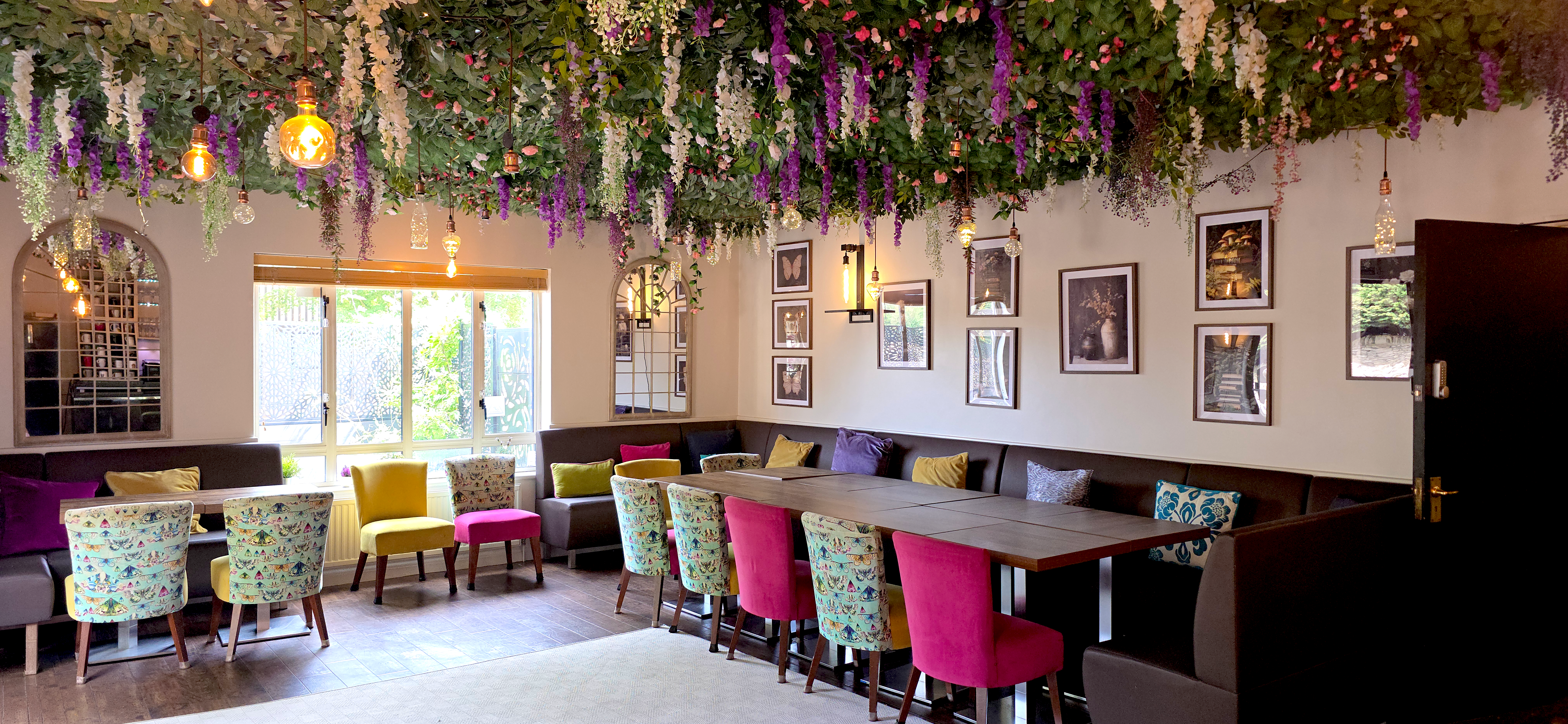 Dining area with banquette seating and coloured chairs under a floral ceiling display