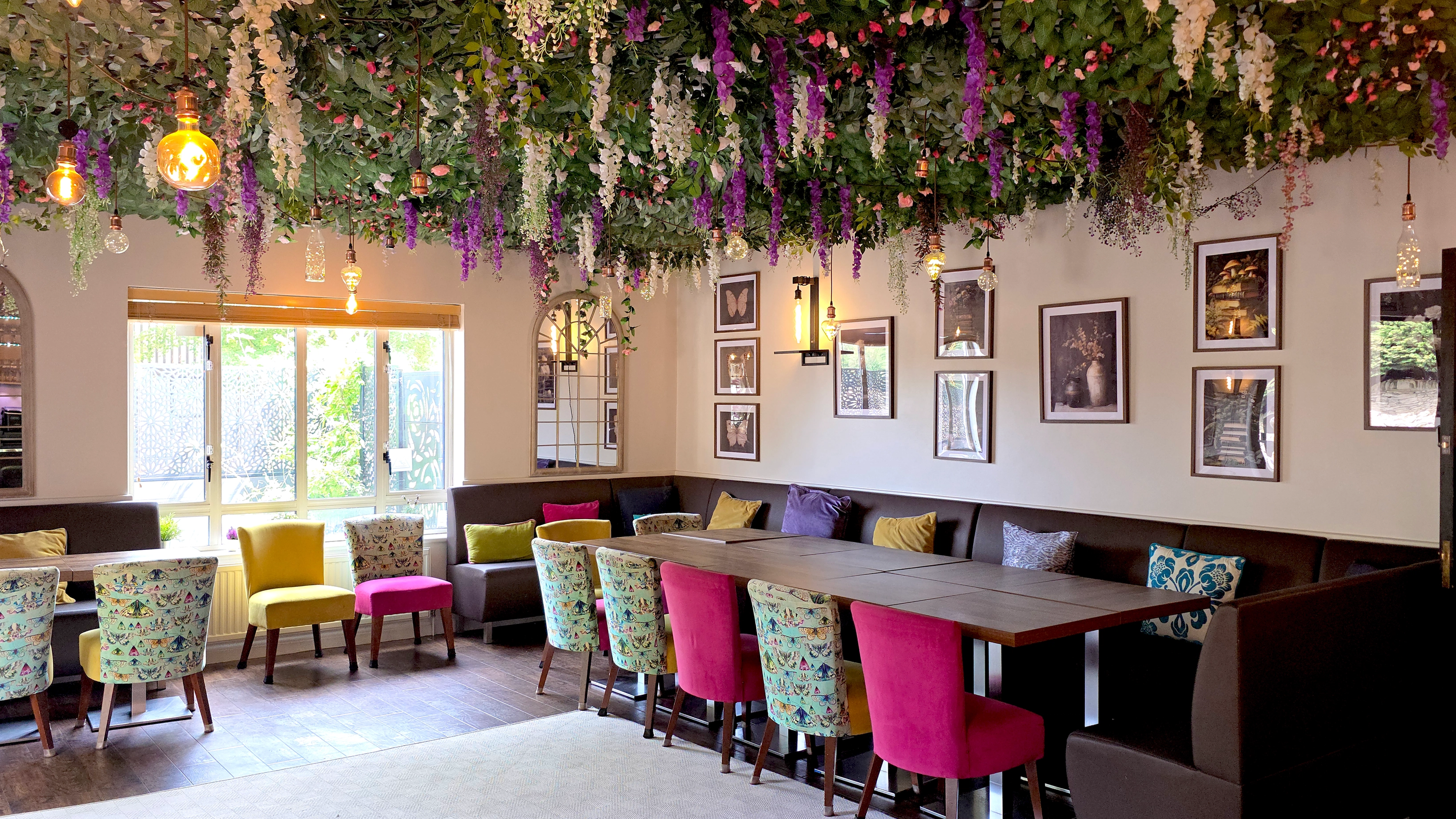 Dining area with banquette seating and coloured chairs under a floral ceiling display