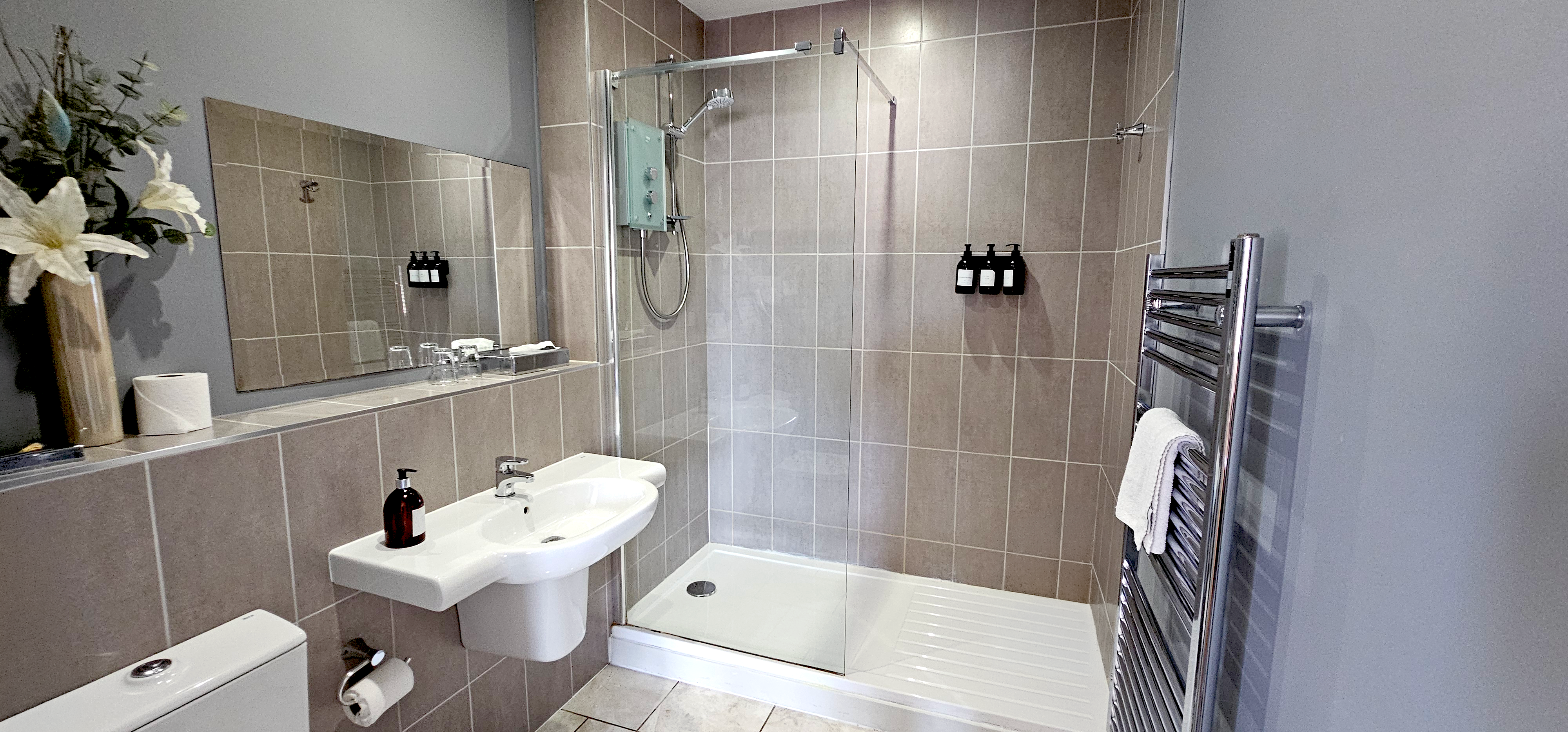 Walk-in shower with glass screen next to a wall-hung basin heated chrome towel rail
