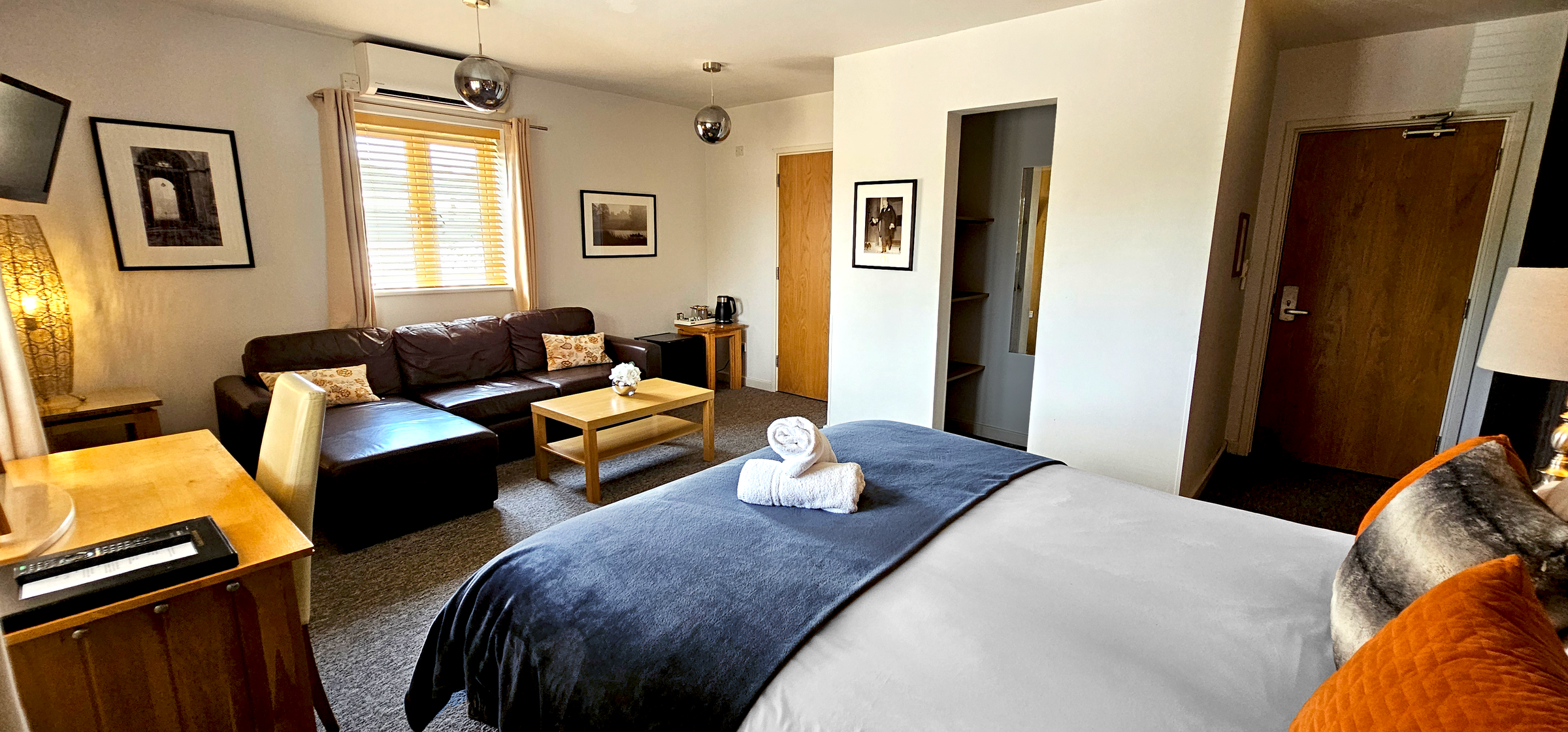 Large deluxe room with a king size bed, brown leather corner sofa, coffee table & desk