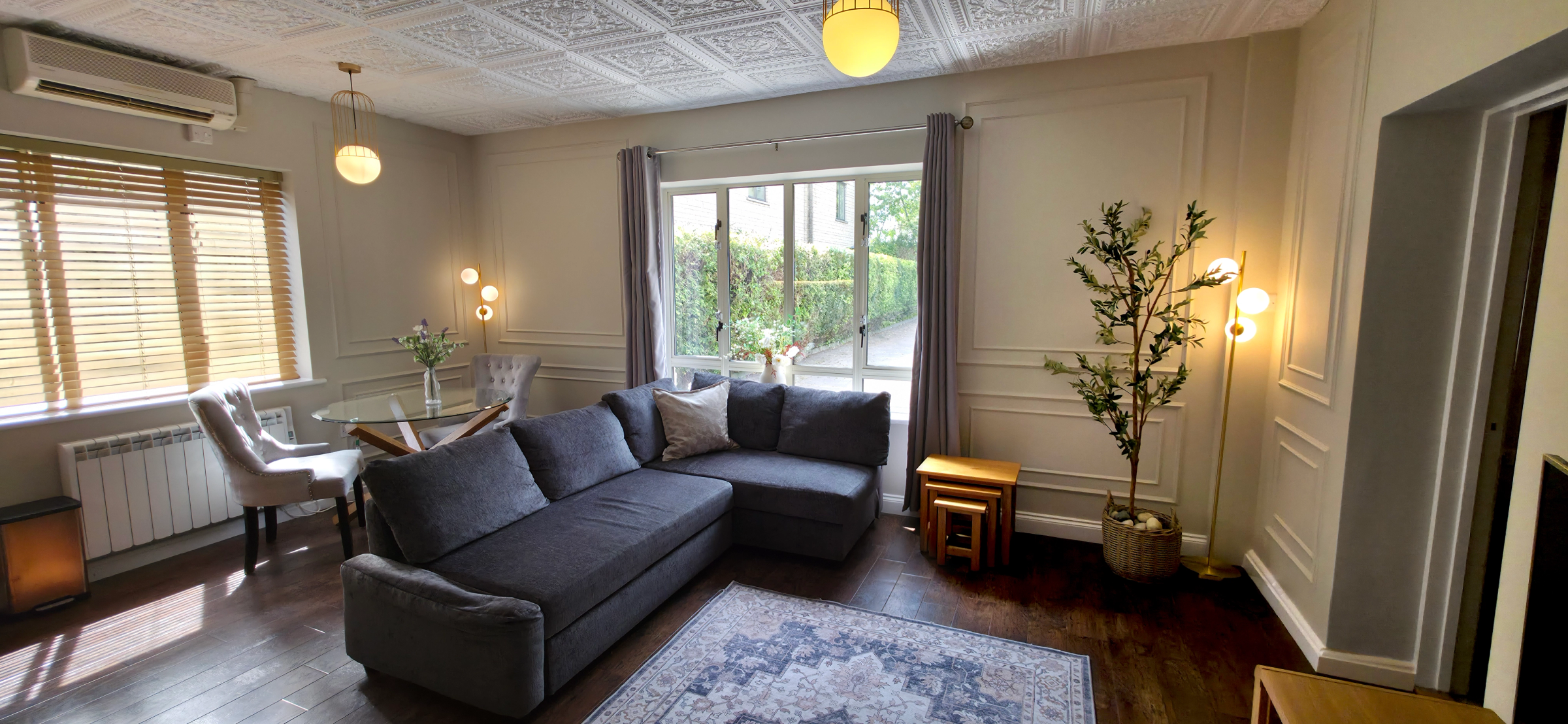 Grey corner sofa with patterned rug glass dining table & a door to the bedroom