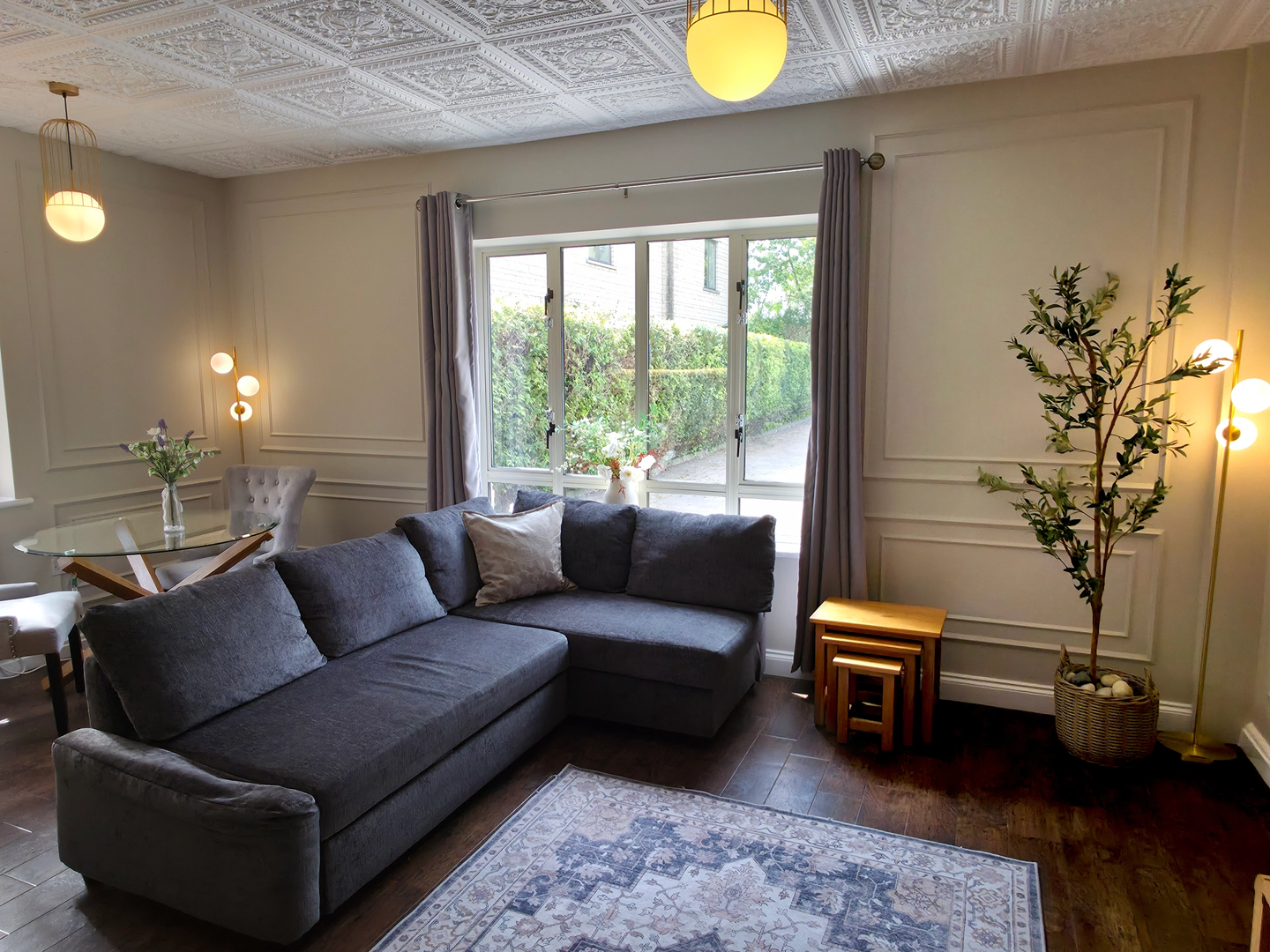 Grey sofa on a patterned rug beside a panelled wall with glass dining table