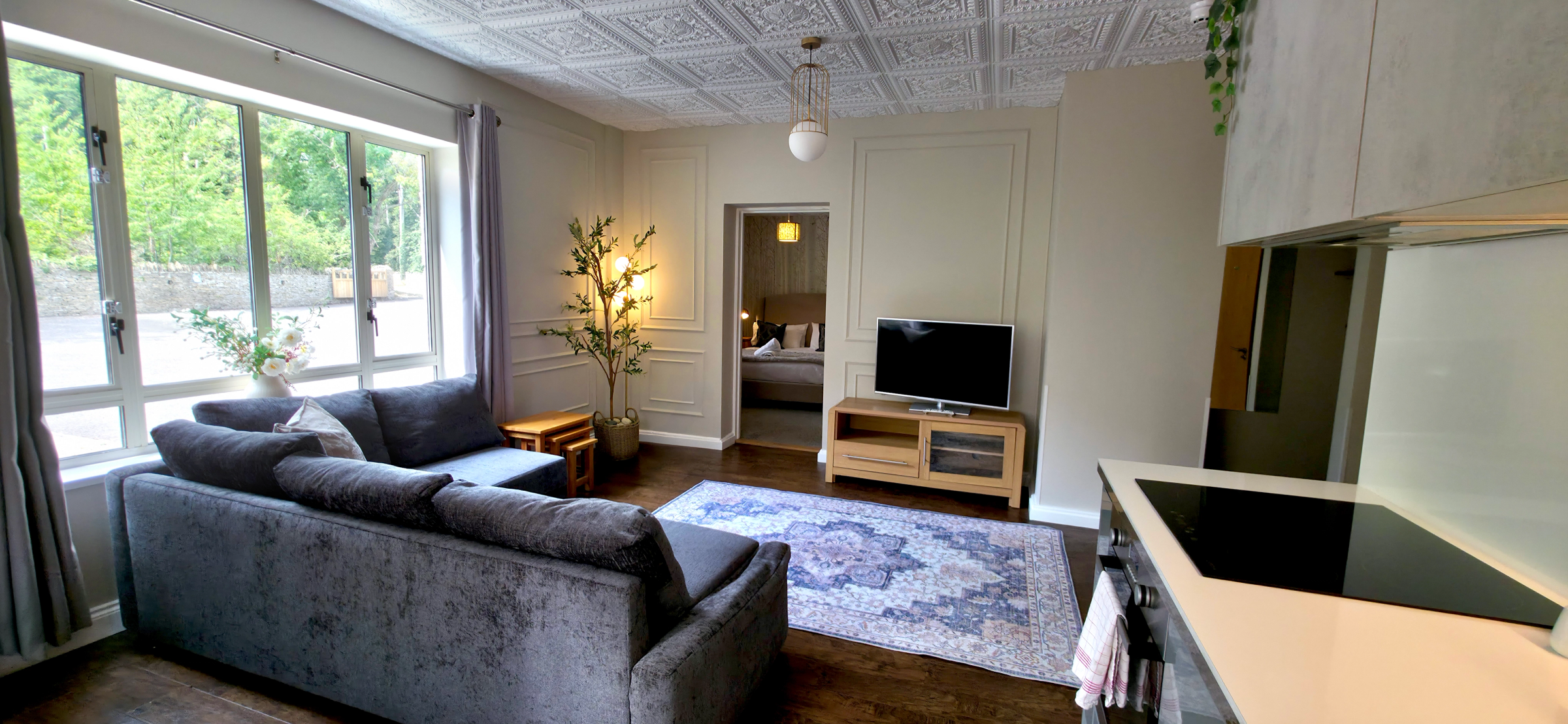 Grey corner sofa facing digital TV, patterned rug & bedroom door with kingsize bed