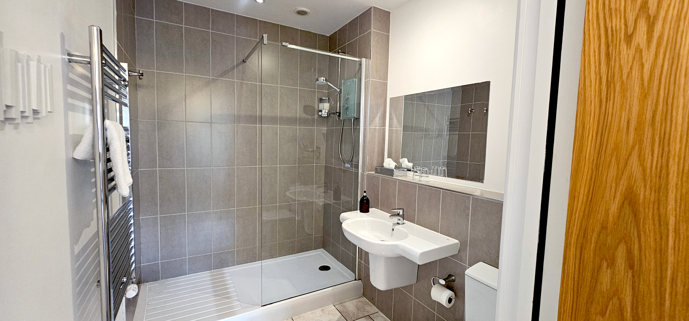 Deluxe walk-in shower with glass screen beside wall-hung basin, mirror & heated towel rail