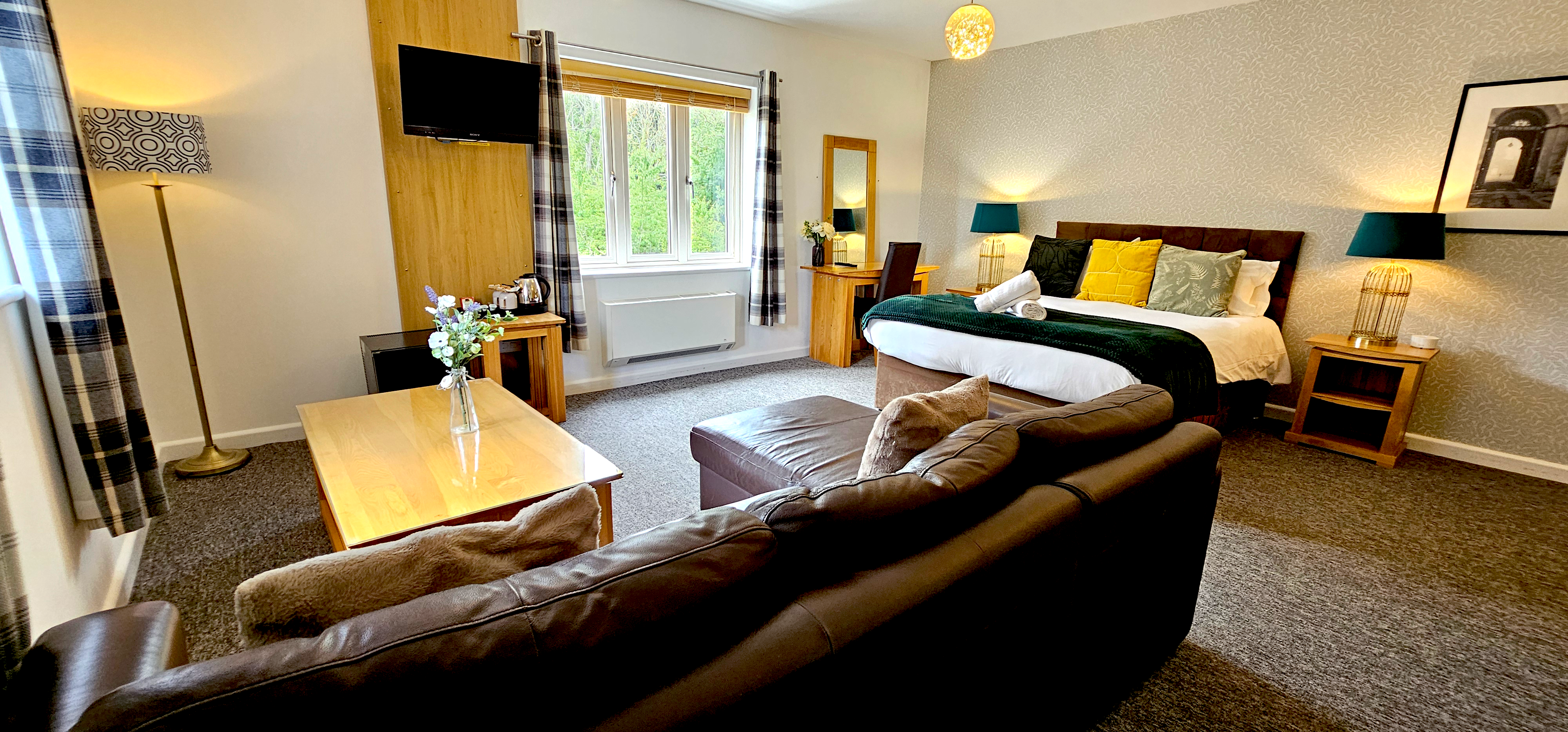 Deluxe king size bed with green throw, rolled towels & matching teal lamps with leather corner sofa, digital TV & coffee table