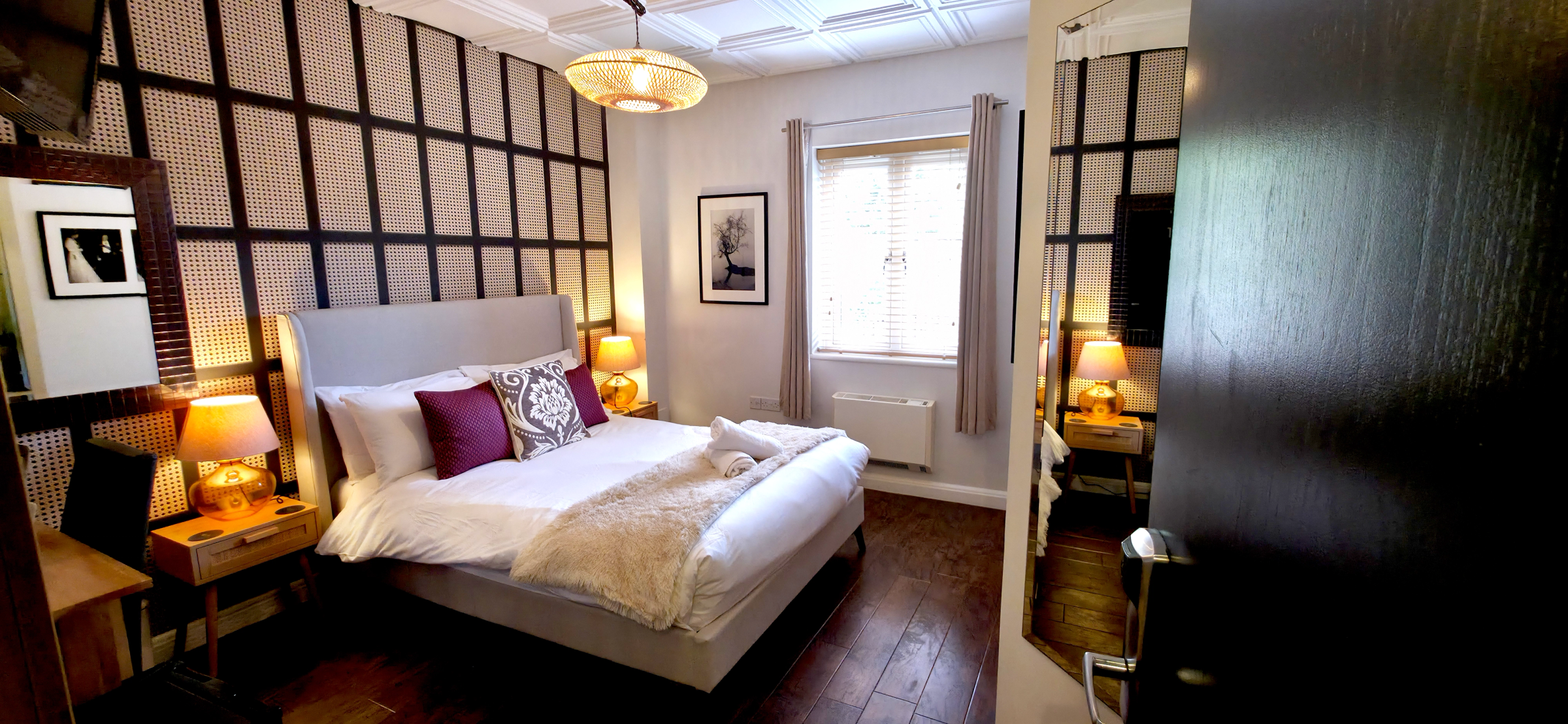 Double bed with faux fur throw and rolled towels against a dark grid wall