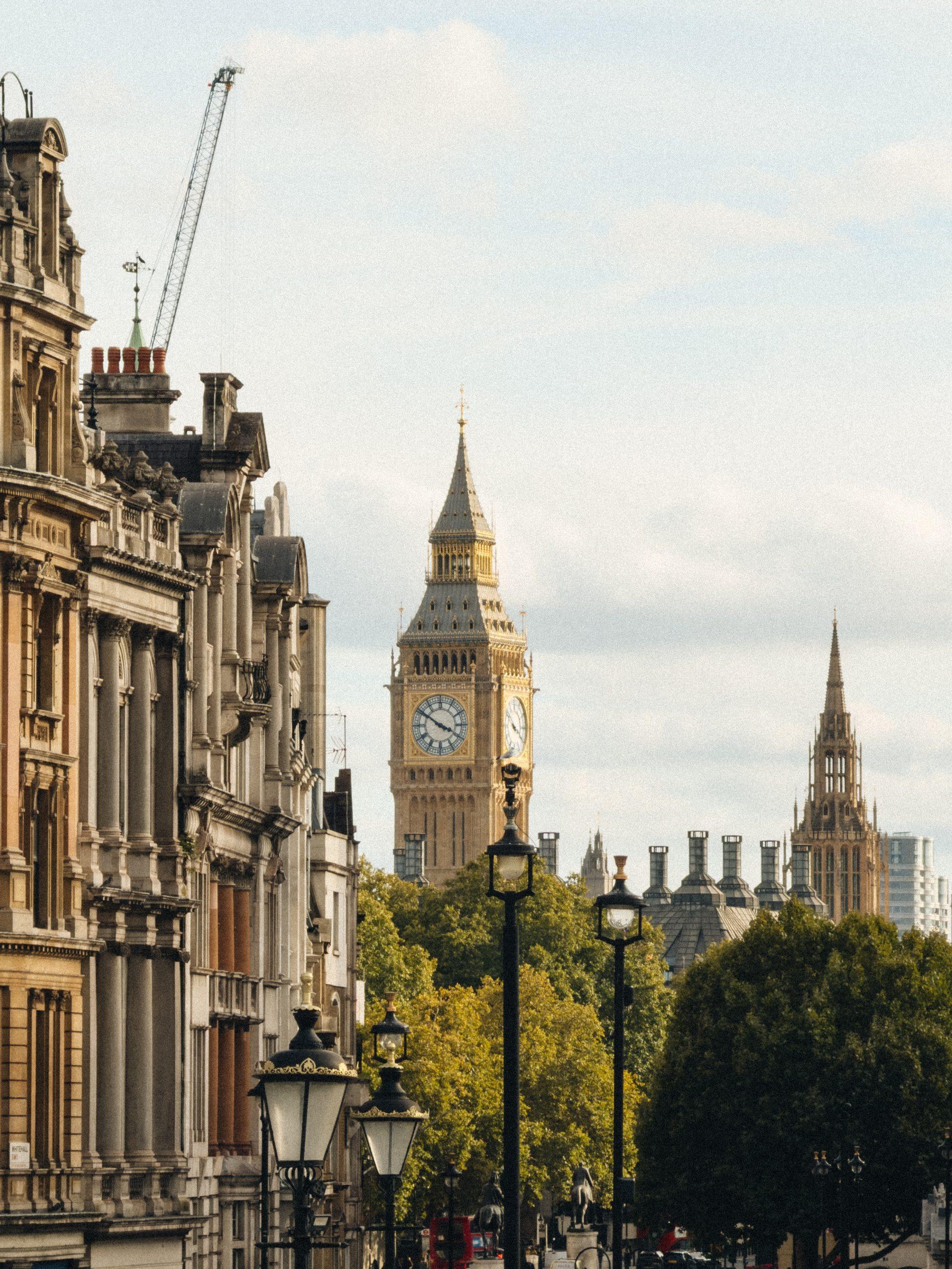 Big Ben and Victoria Tower seen down a London street lined with lamp posts and trees