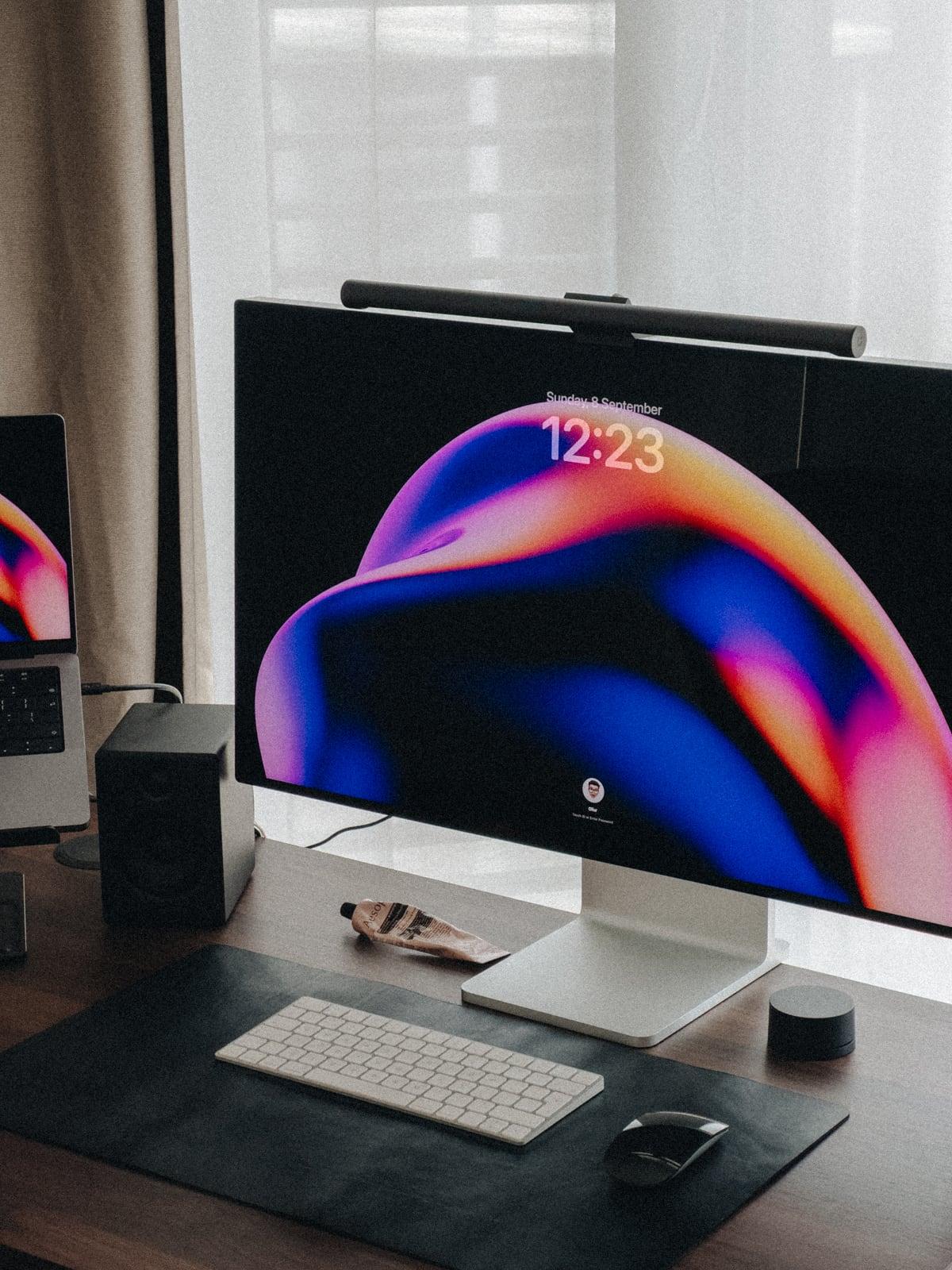 Desk setup with a monitor showing a colourful swirled lock screen, keyboard and mouse
