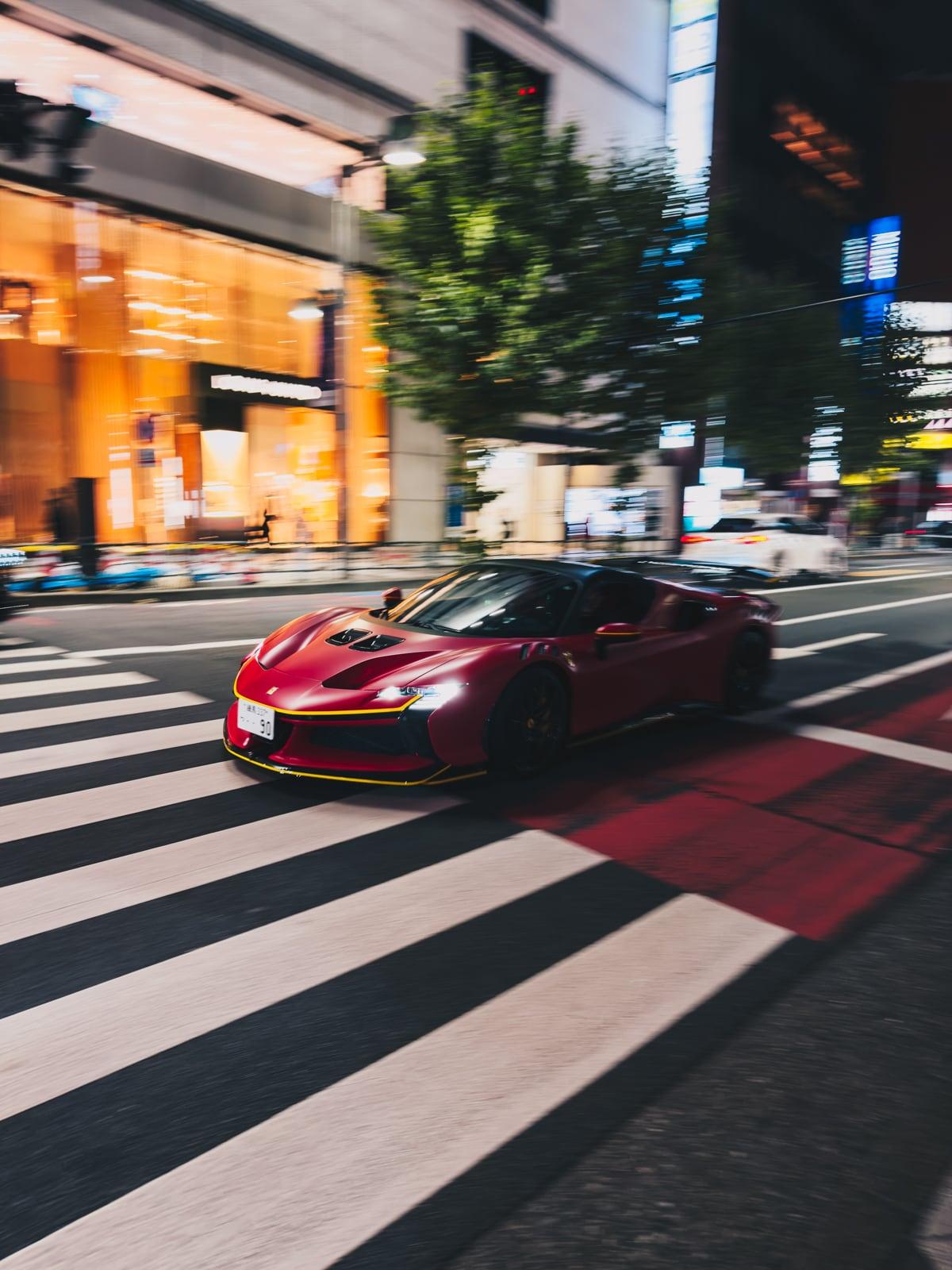 Red Ferrari captured with motion blur crossing a striped pedestrian crossing on a city street at dusk