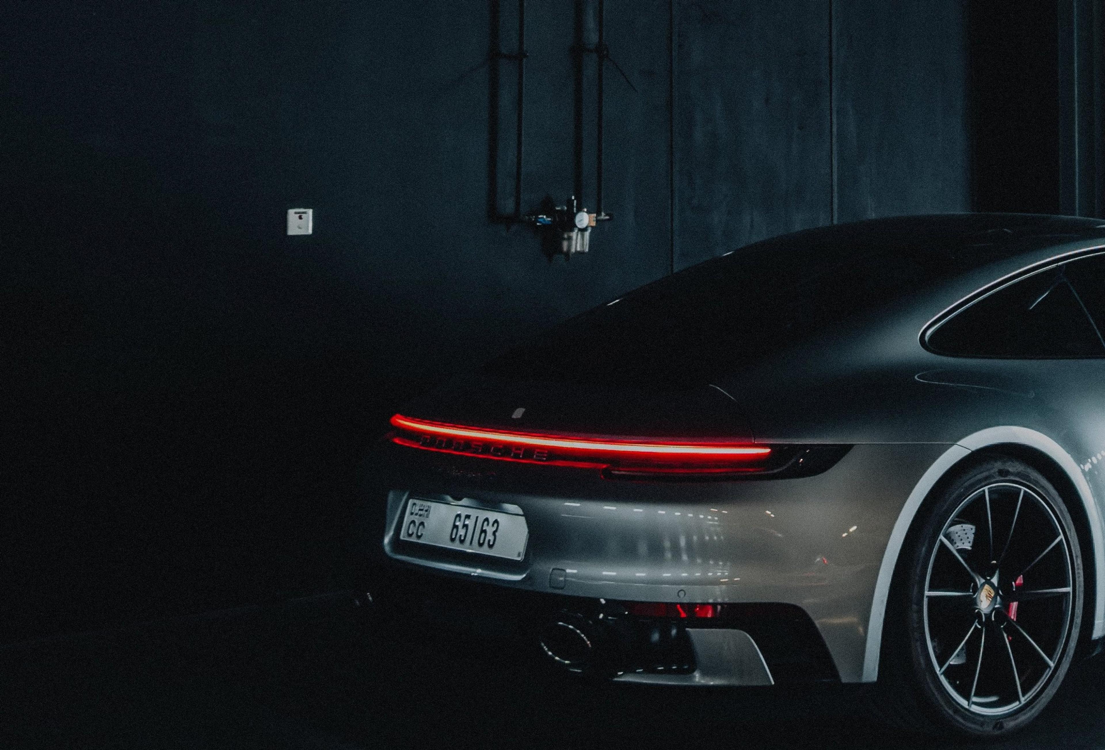 A sports car's rear end glowing with a red tail light in a dim, moody garage