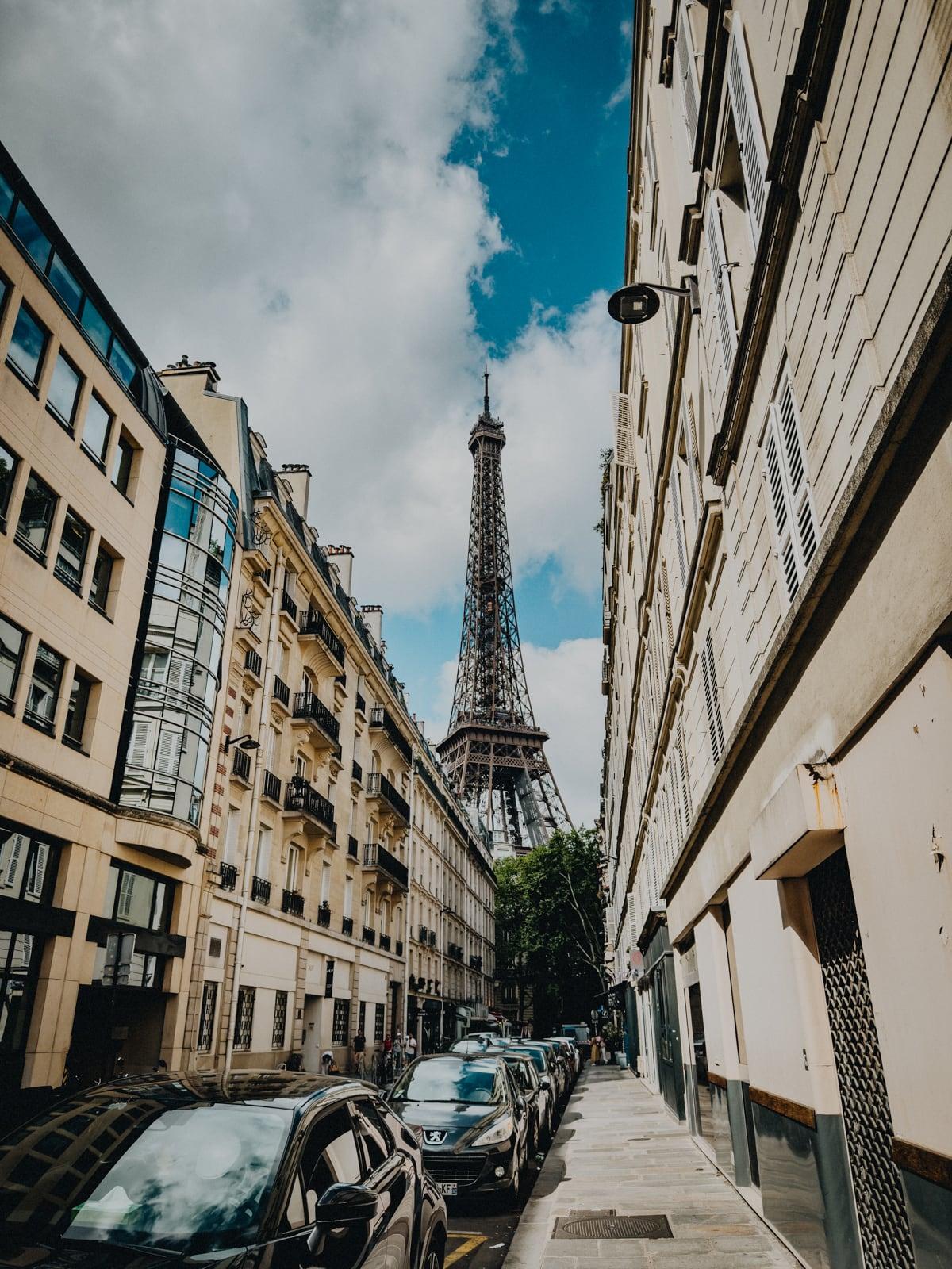 Eiffel Tower framed at the end of a narrow Parisian street lined with cream buildings and parked cars