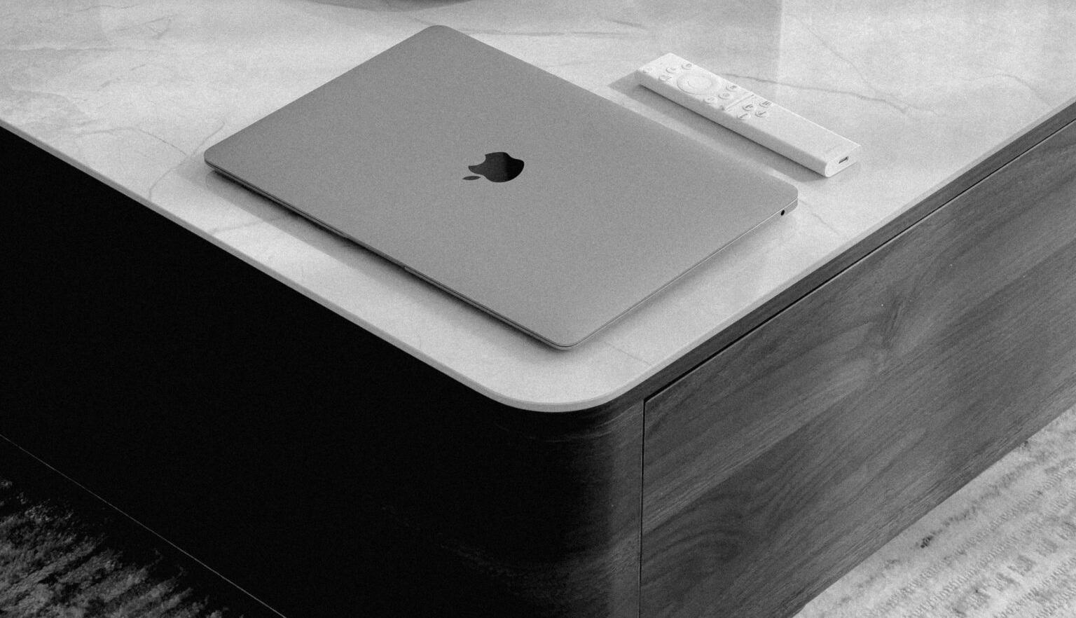 Monochrome shot of a MacBook and remote resting on a marble table corner