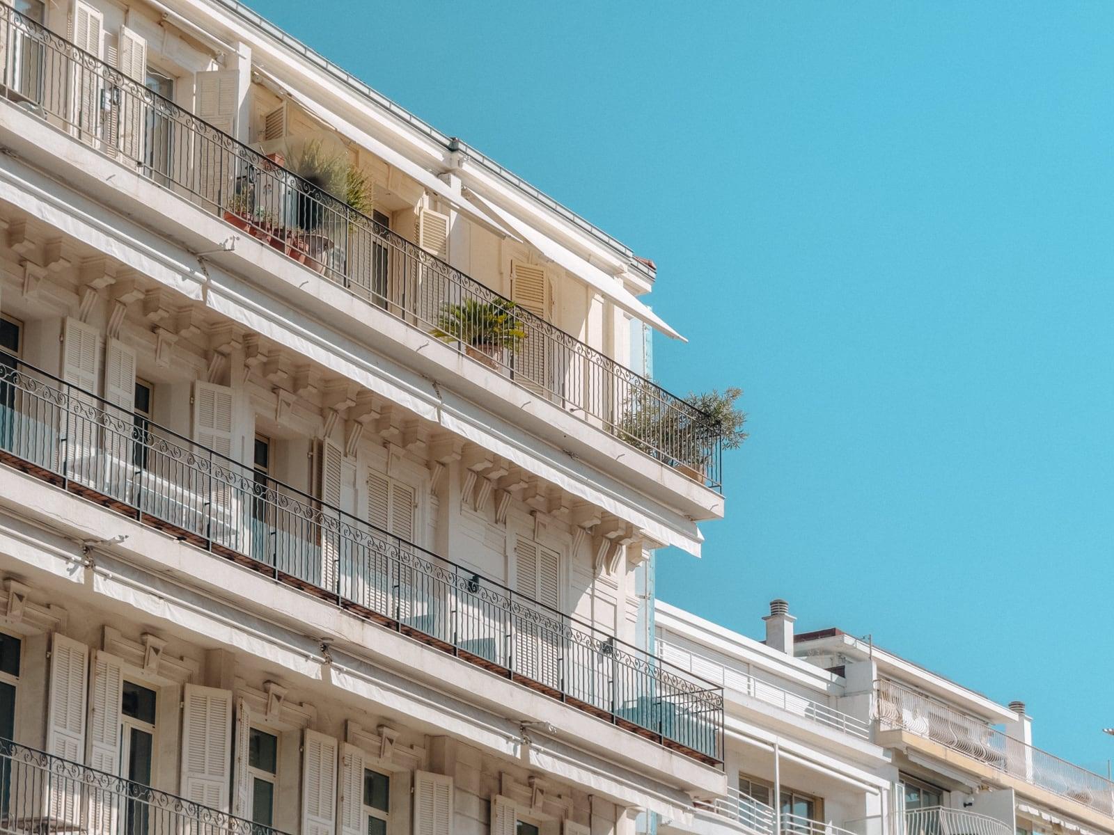 A white balconied apartment building against a bright blue sky