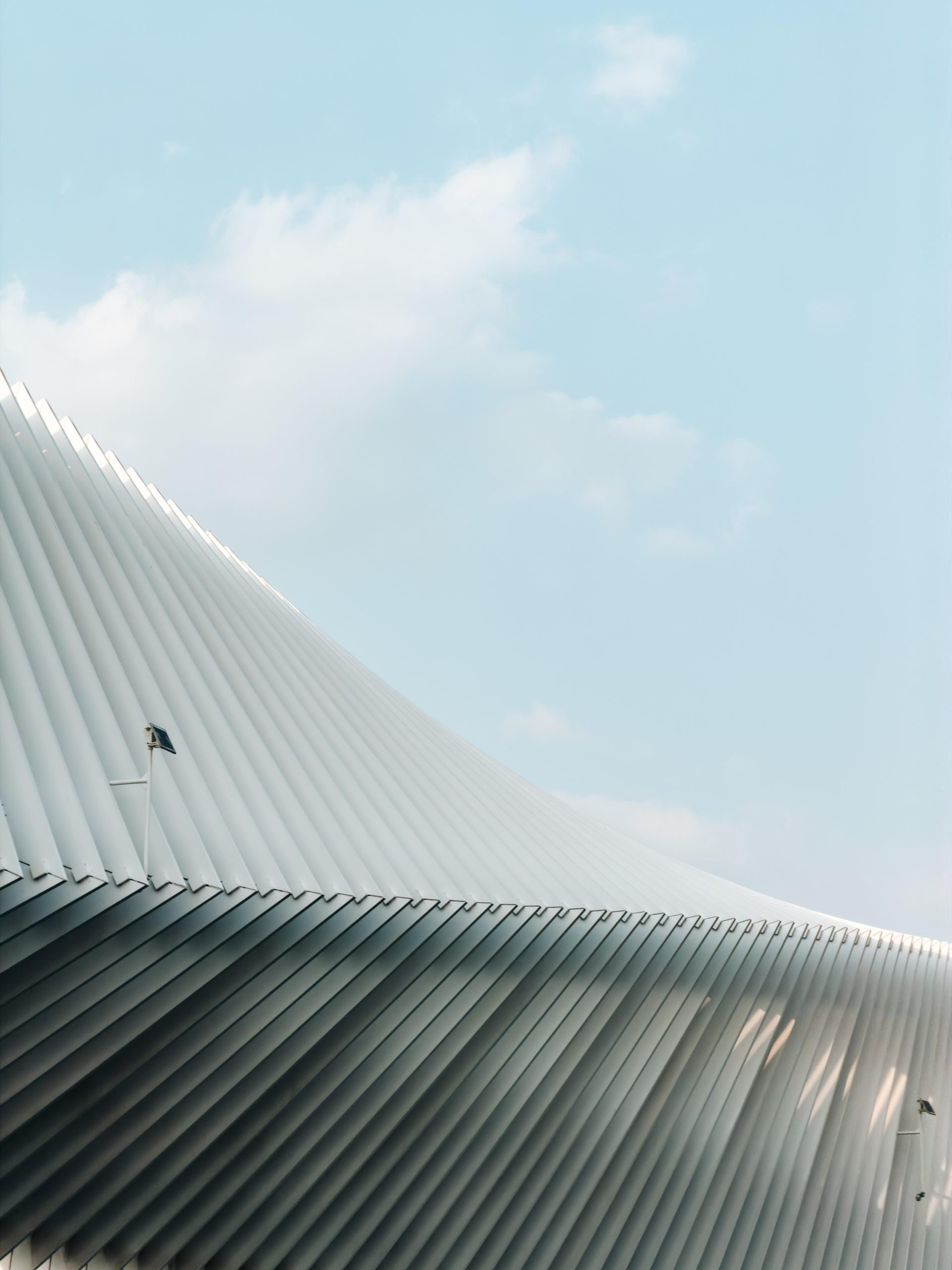 A pleated white canopy roof curving against a pale blue sky with wispy clouds
