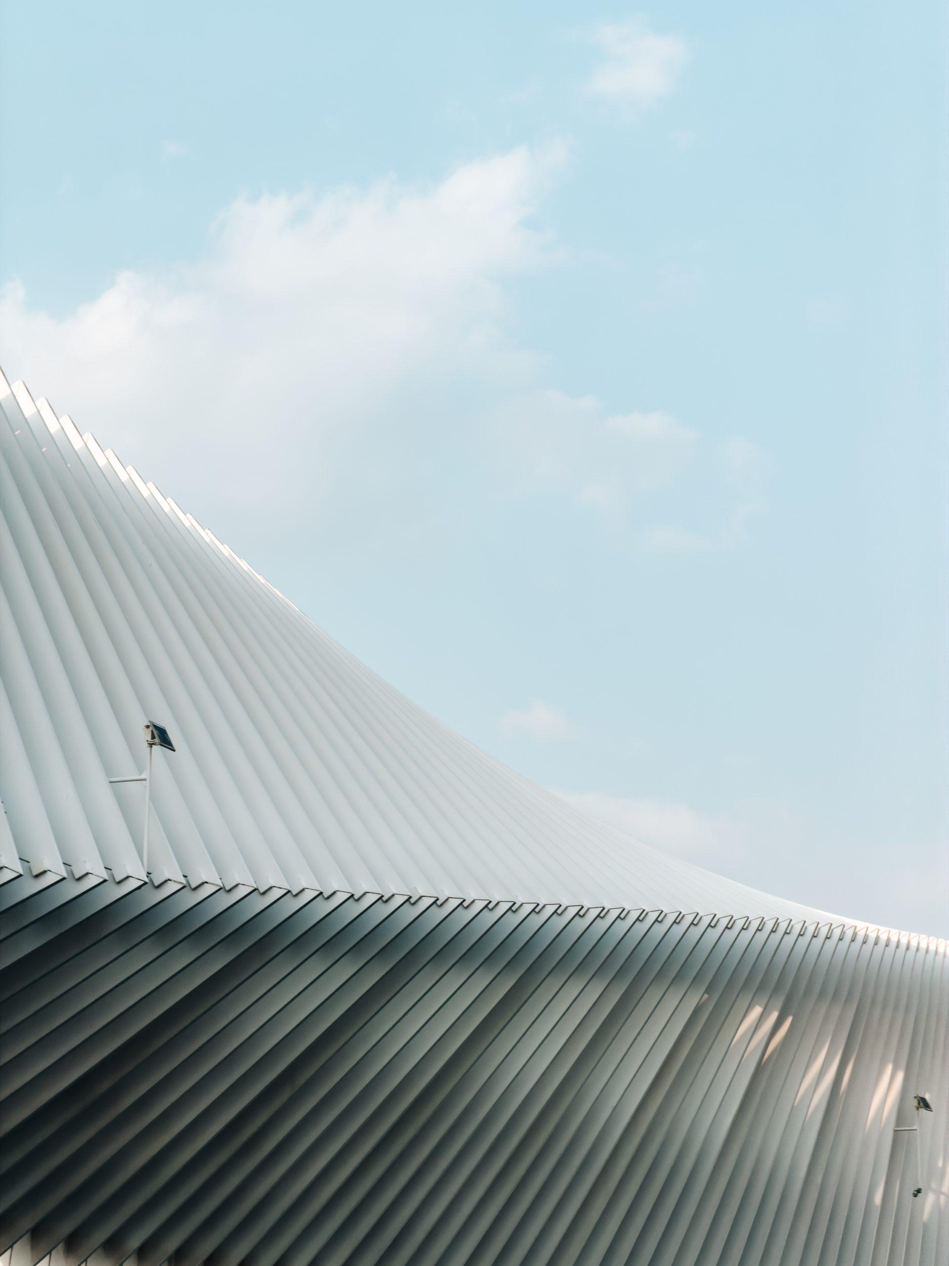 A pleated white canopy roof curving against a pale blue sky with wispy clouds