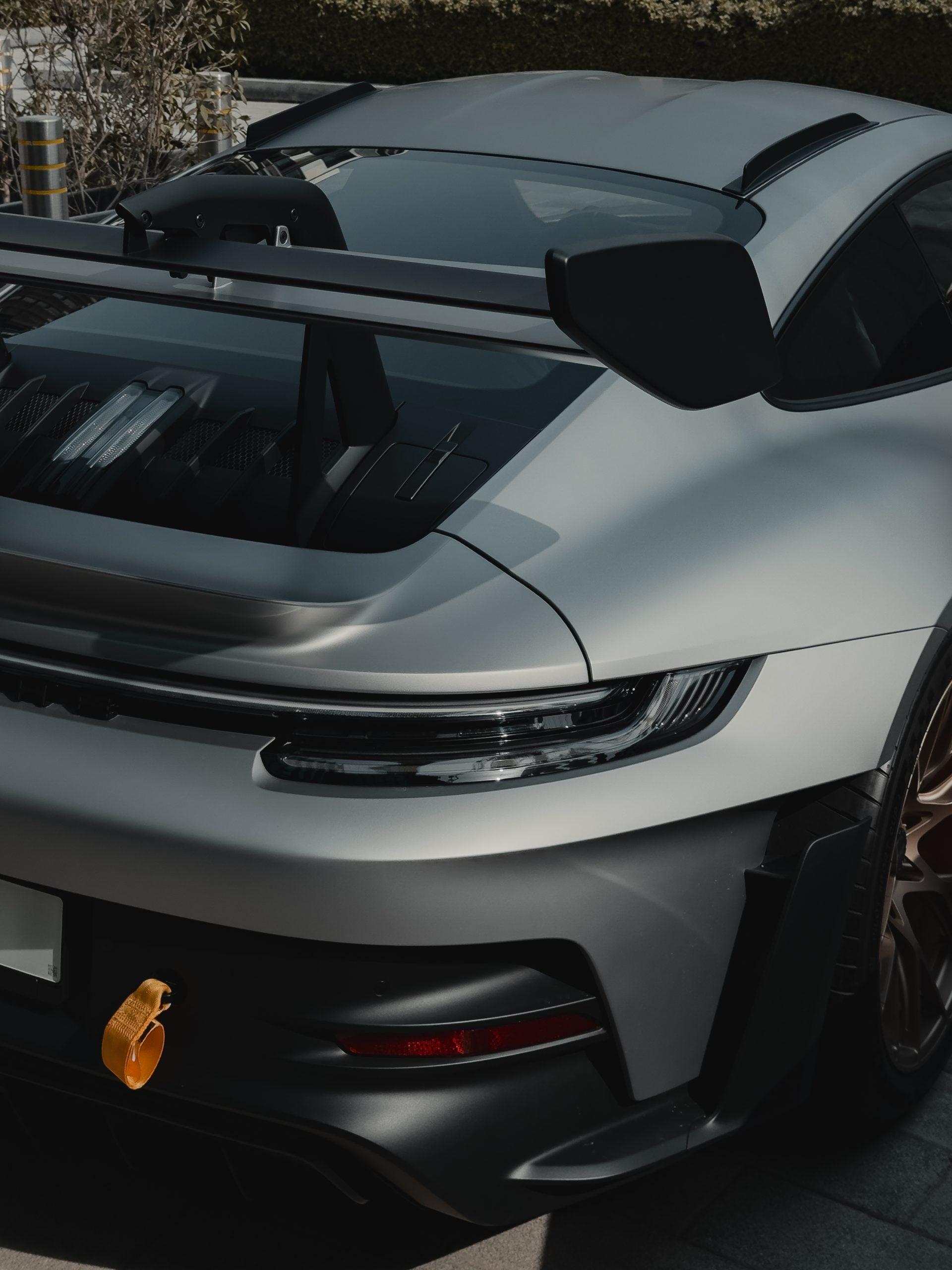 Close-up of a white sports car's rear spoiler and taillight with an orange tow strap