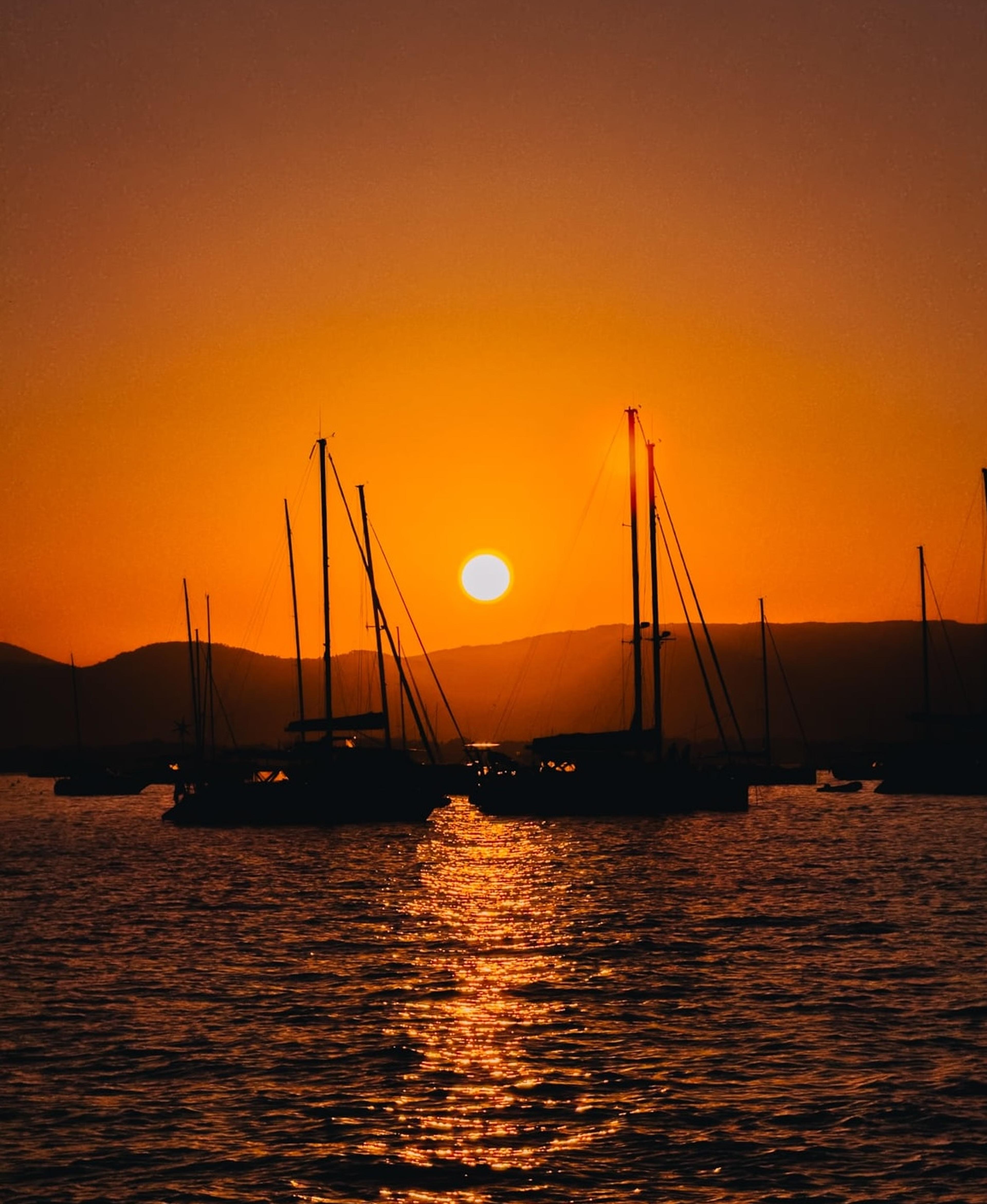 Sailboats silhouetted against a bright orange sunset over calm water