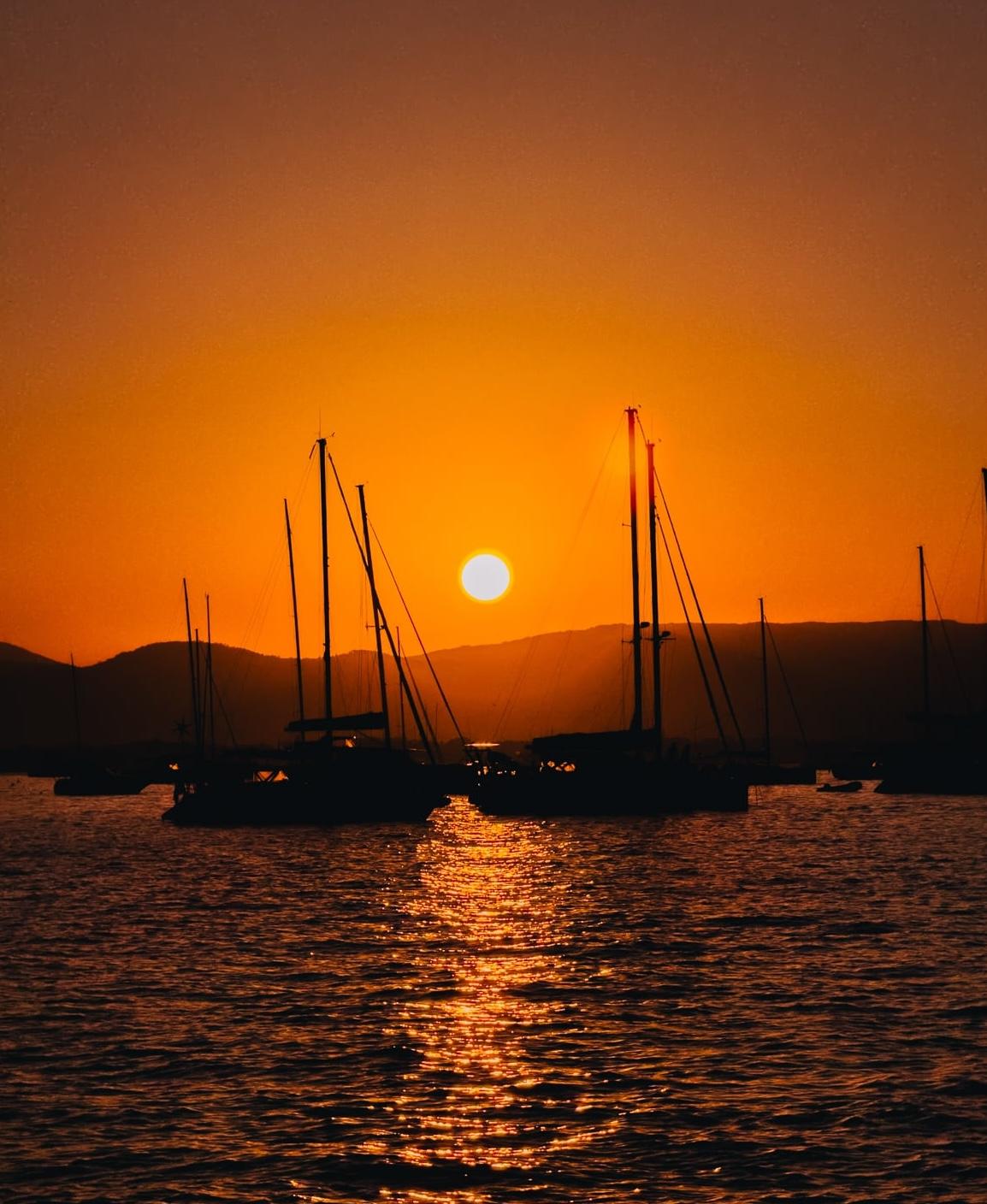 Sailboats silhouetted against a bright orange sunset over calm water