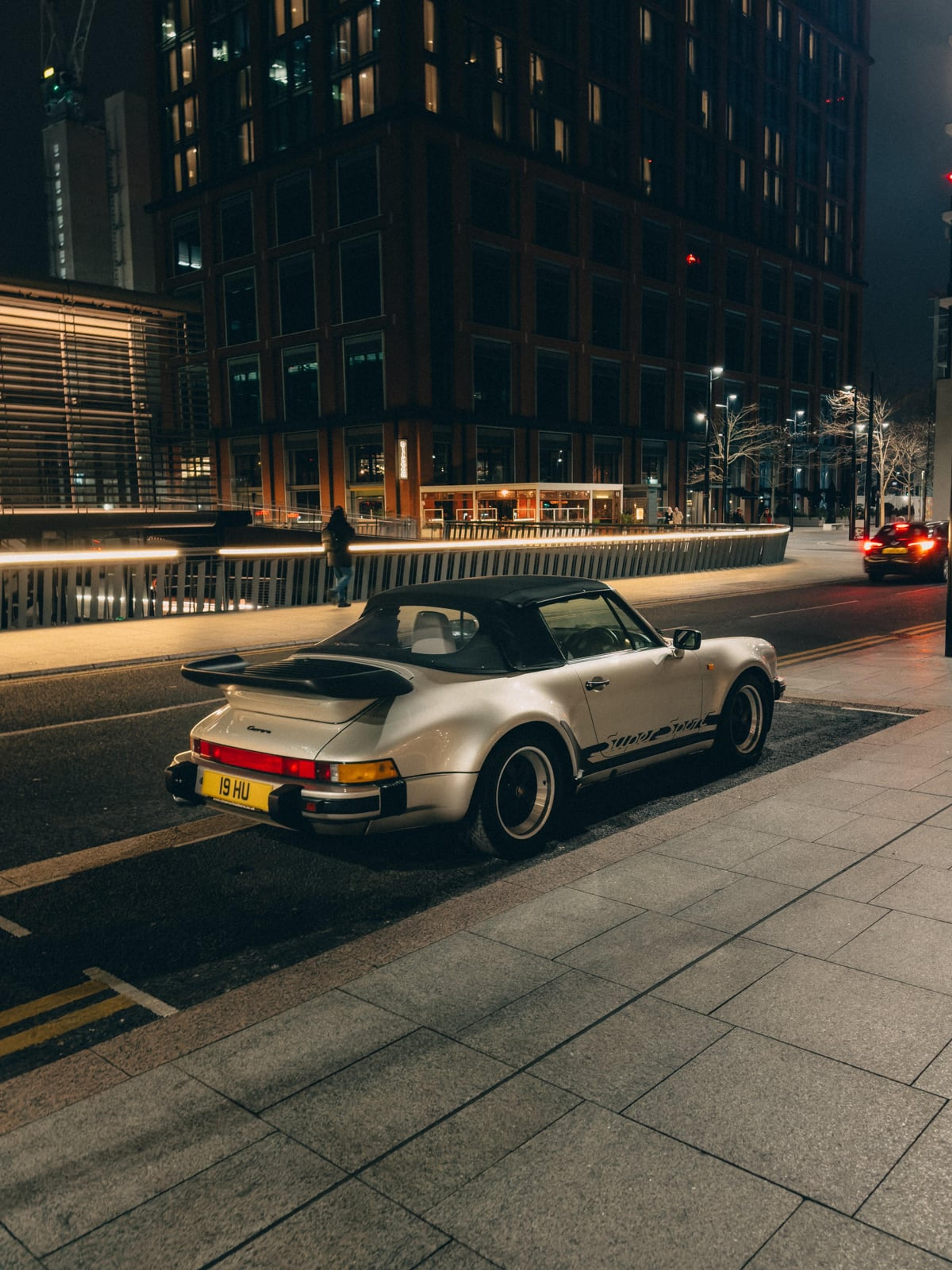 Classic white convertible Porsche parked on a city street at night with grainy flash lighting