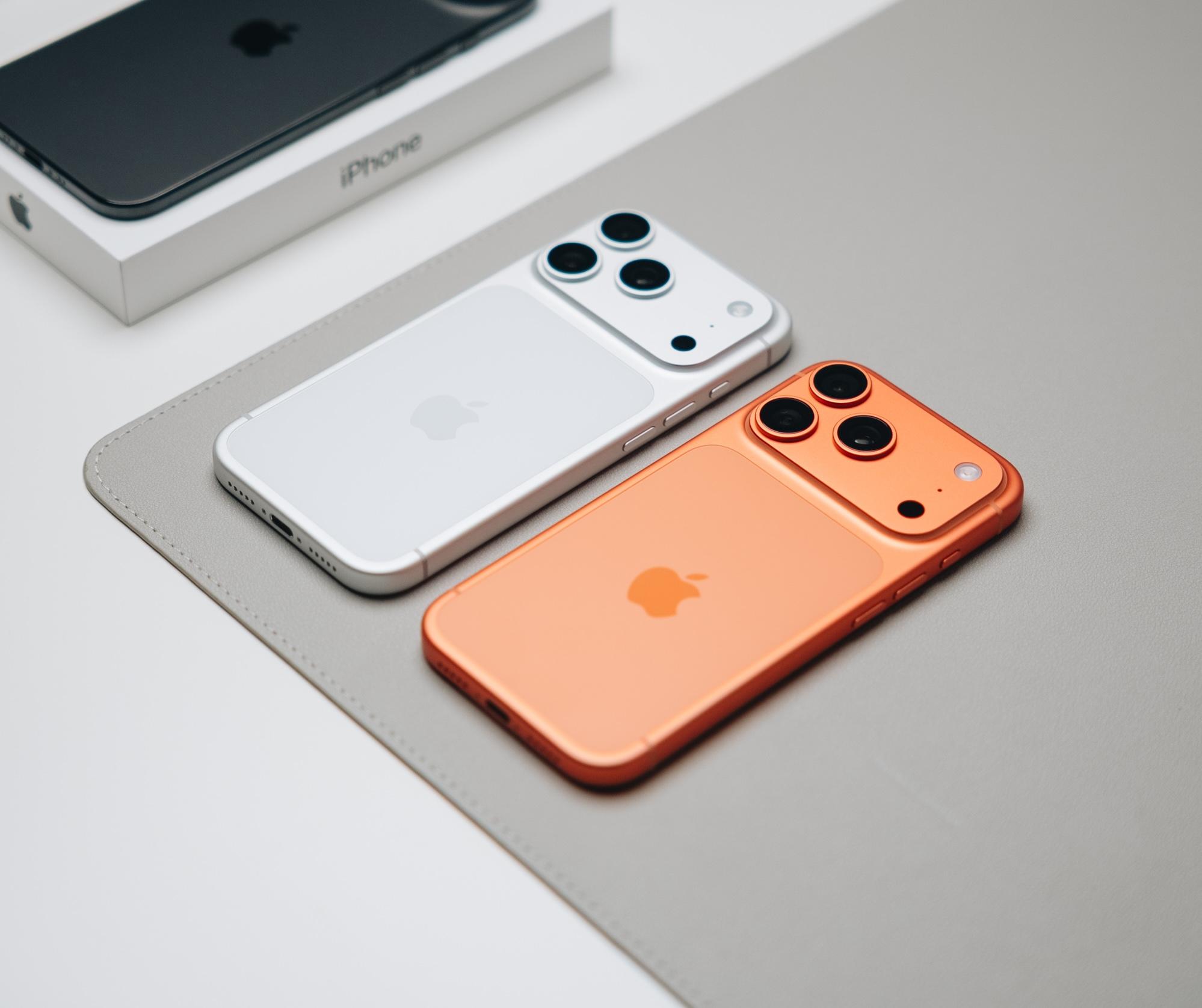 White and orange iPhones lying side by side on a desk next to their retail box