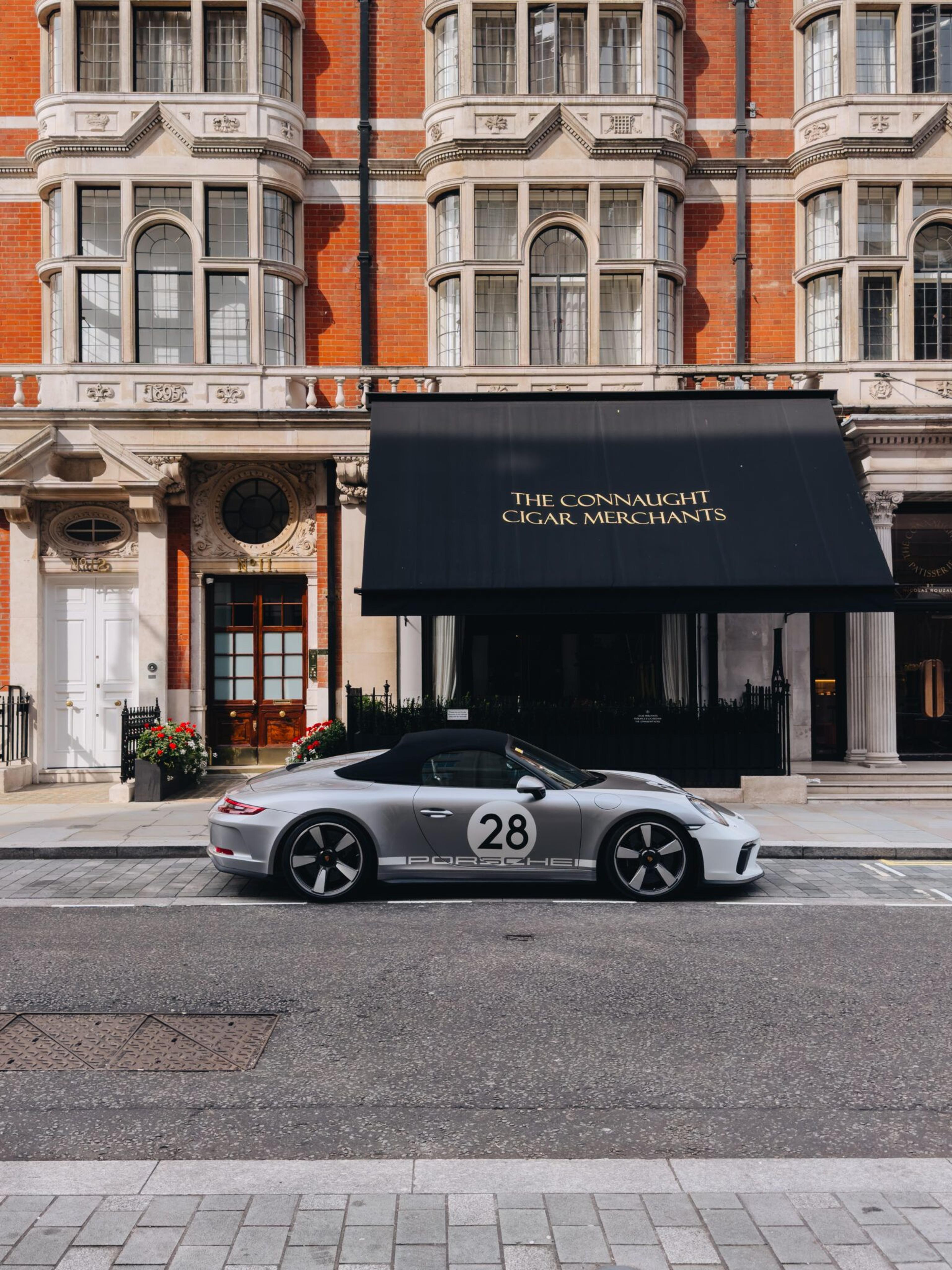 Silver Porsche 911 parked outside a red-brick building with a black awning reading 'The Connaught Cigar Merchants'