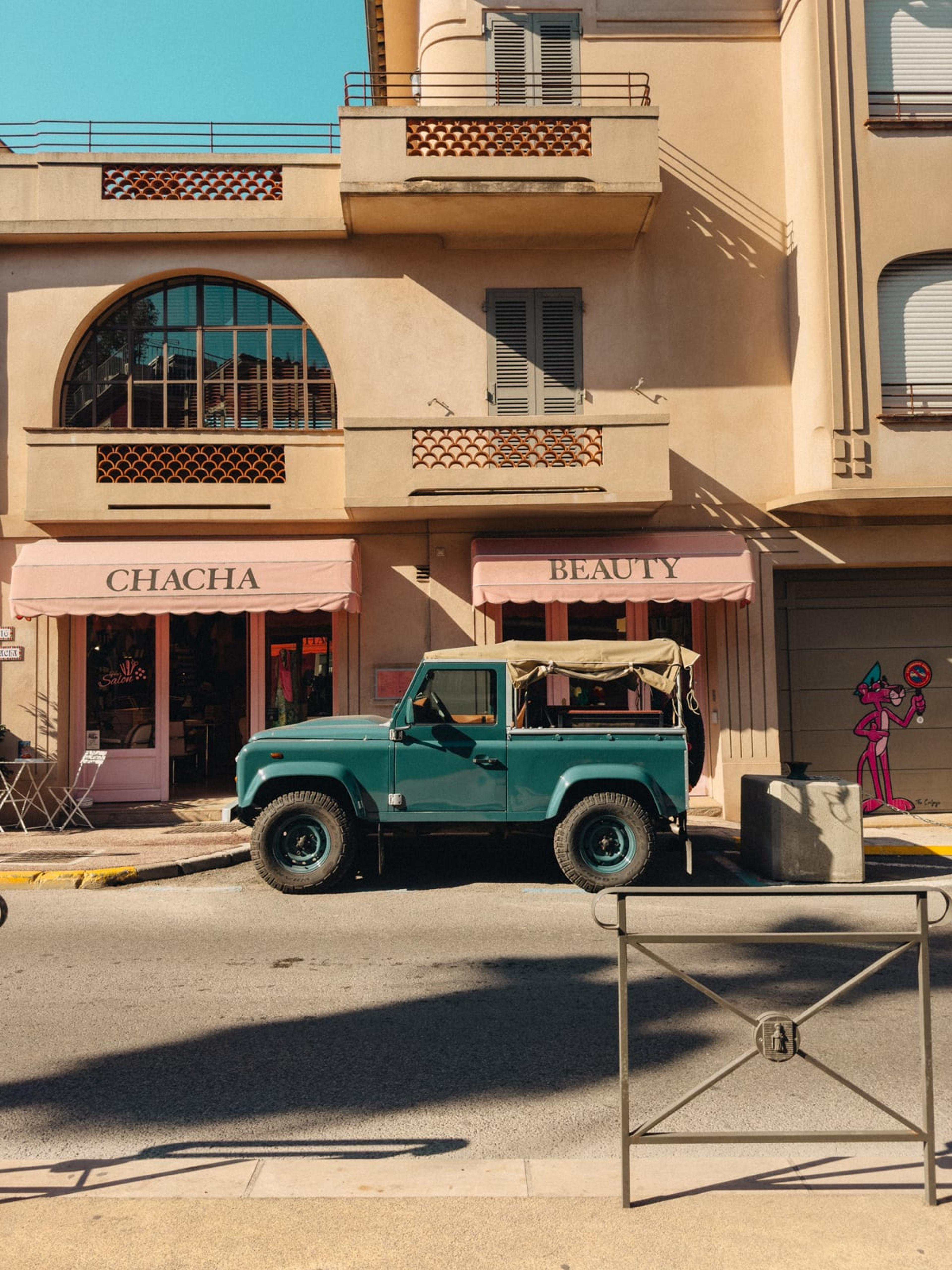 Overexposed street scene with a teal jeep parked outside pastel pink shopfronts