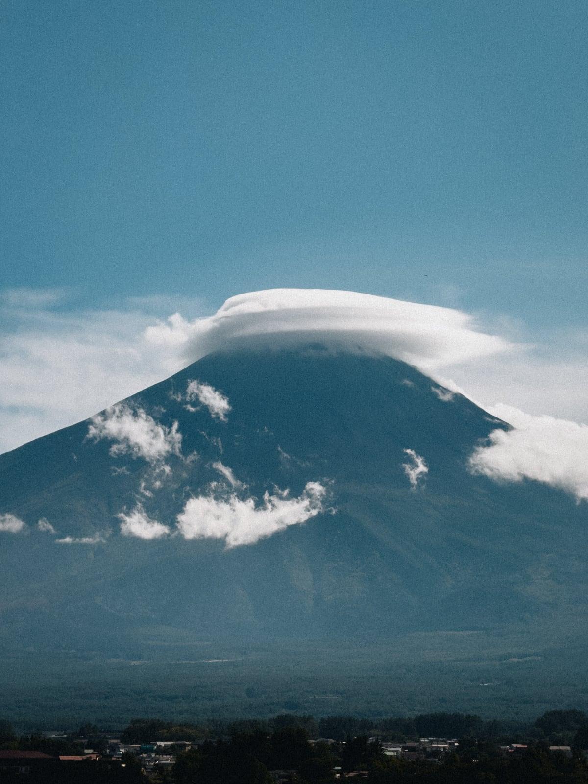 Mount Fuji capped by a lens-shaped cloud, blue sky and hazy foothills below
