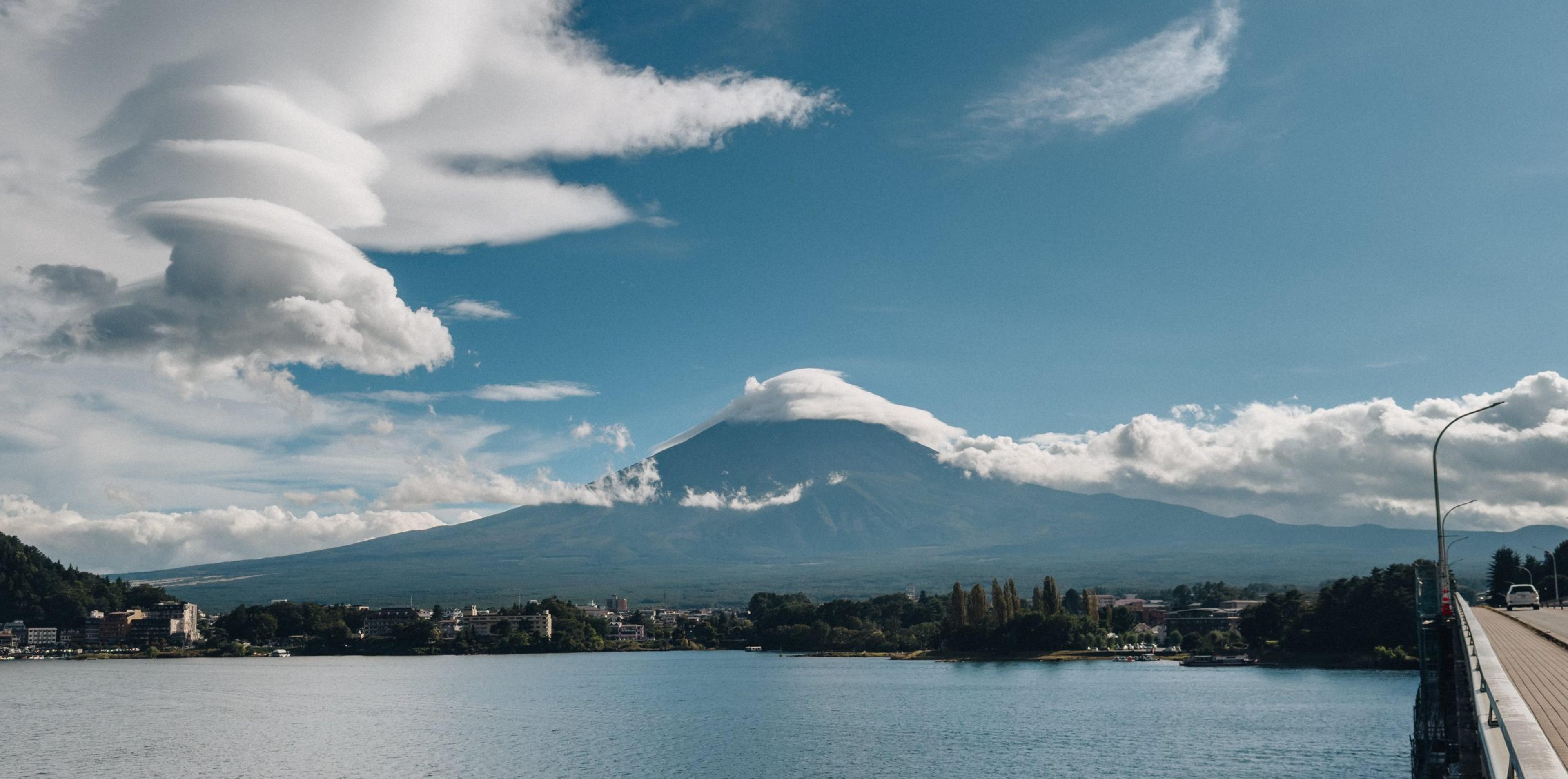 Snow-capped Mount Fuji wrapped in dramatic lenticular clouds above a lake and lakeside town