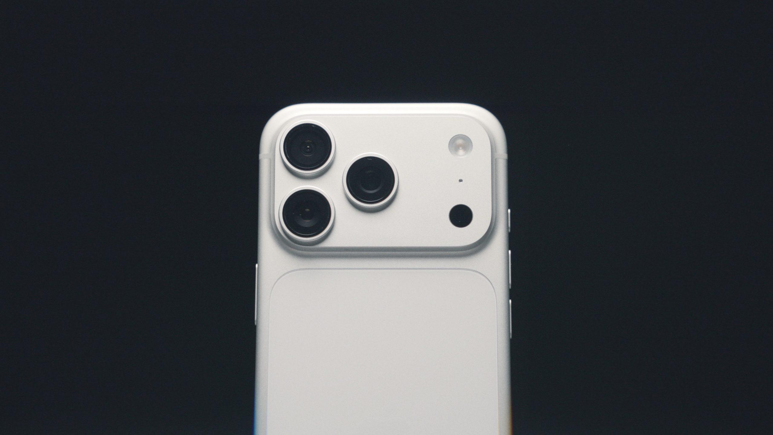 Close-up of an iPhone's triple camera lenses on a white phone against a dark background
