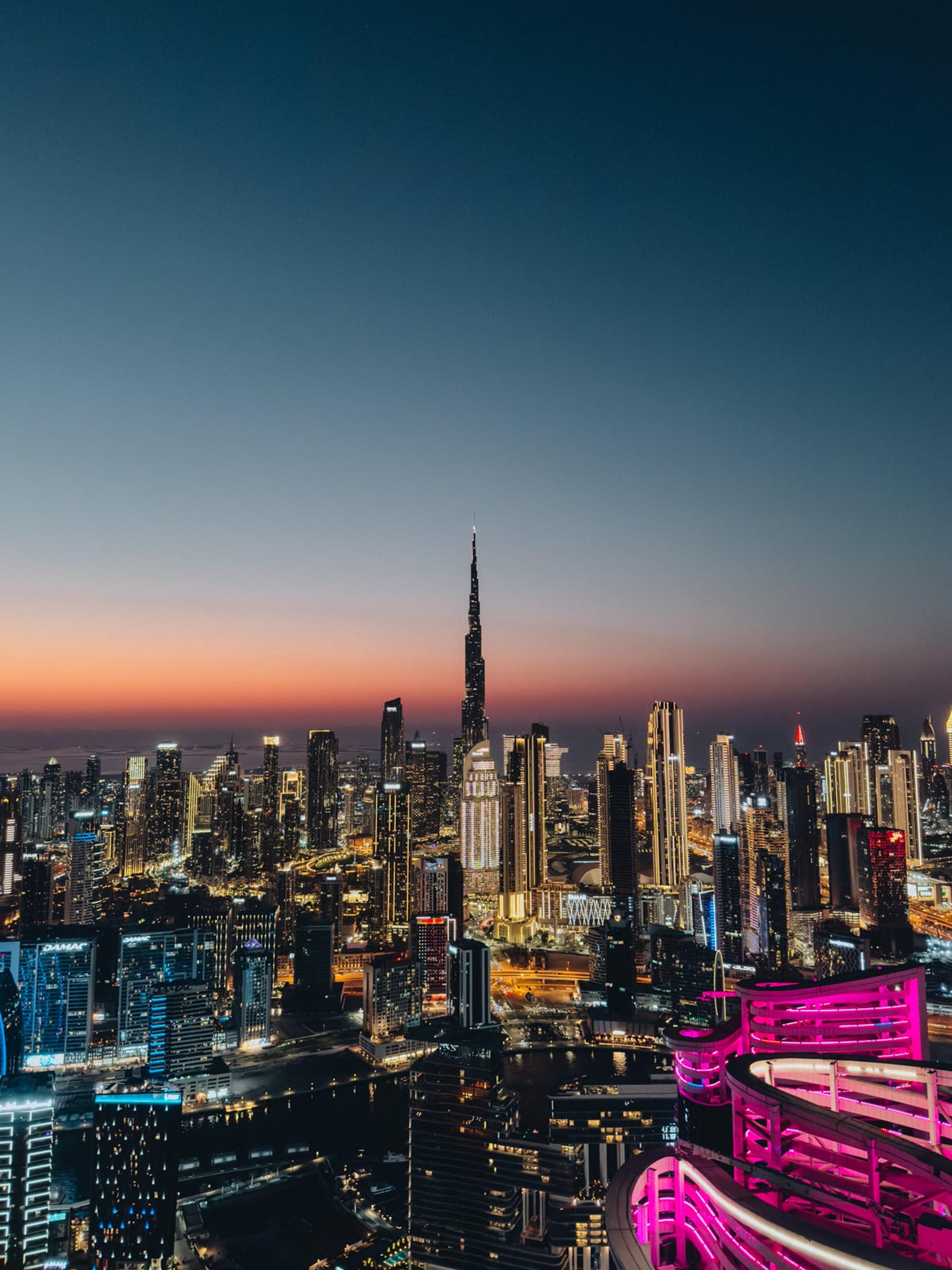 Dubai skyline at dusk with the Burj Khalifa lit up and a neon-pink rooftop terrace in the foreground