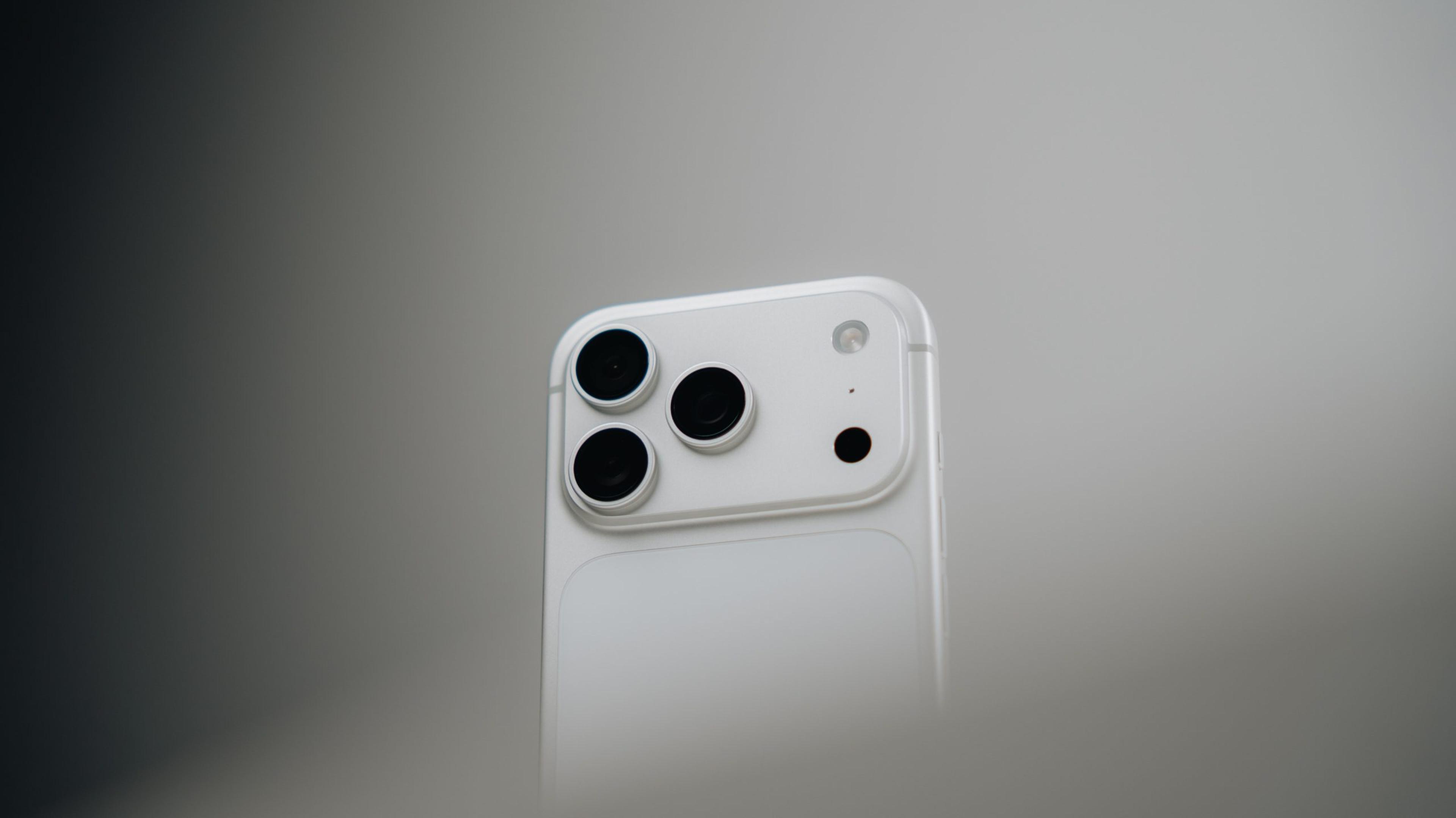 Close-up of a white iPhone's triple camera module against a soft grey background