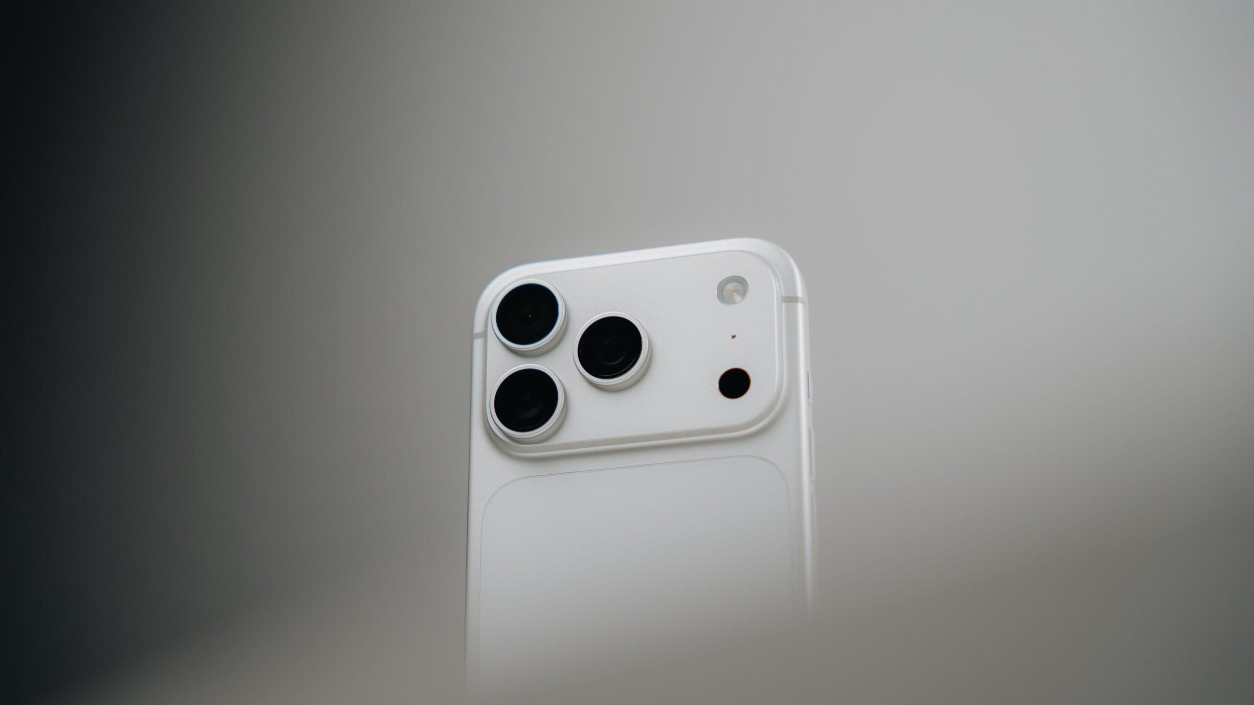 Close-up of a white iPhone's triple camera module against a soft grey background