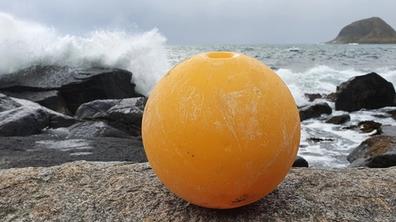Oransje plastkule i fjæra, hav og sjøsprøyt i bakgrunnen.