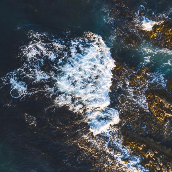 Drone photo of ocean and waves meeting rocks on shore.